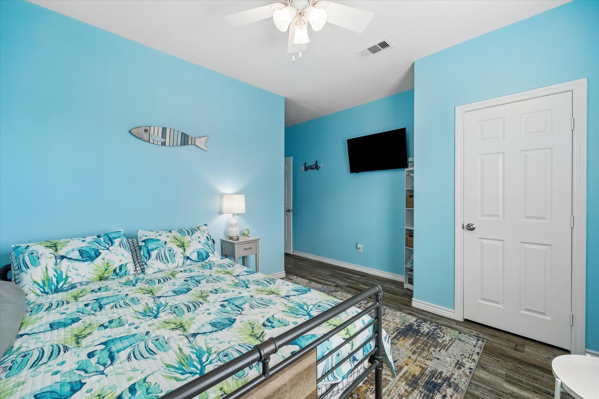Bright and inviting bedroom with coastal-themed decor, featuring a comfortable bed, soothing blue walls, and modern flooring.