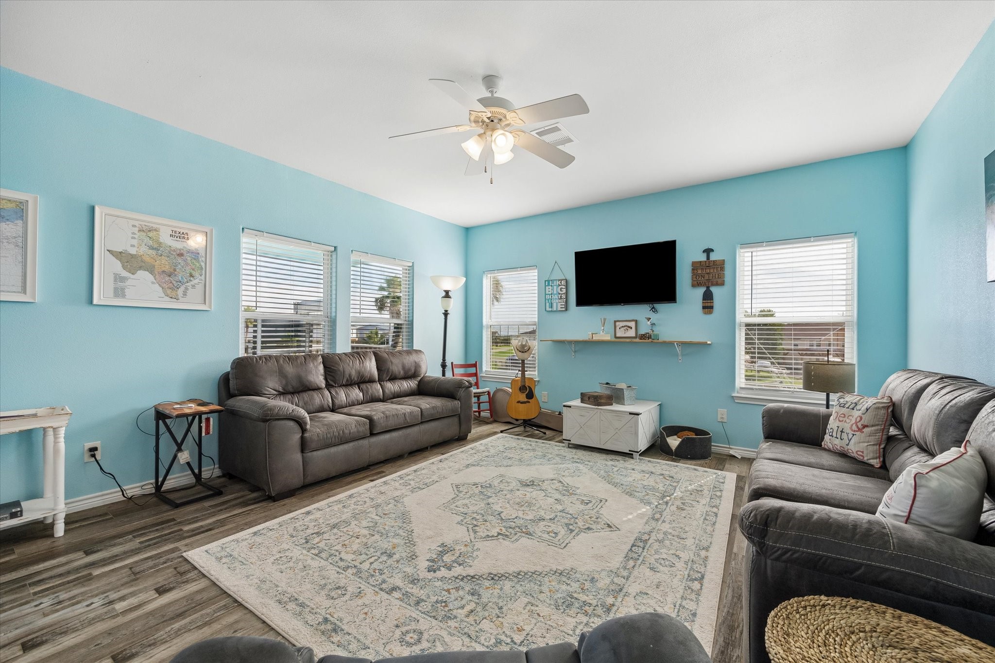 Bright and inviting living room with soft blue walls, ample natural light from multiple windows and a ceiling fan for comfort.