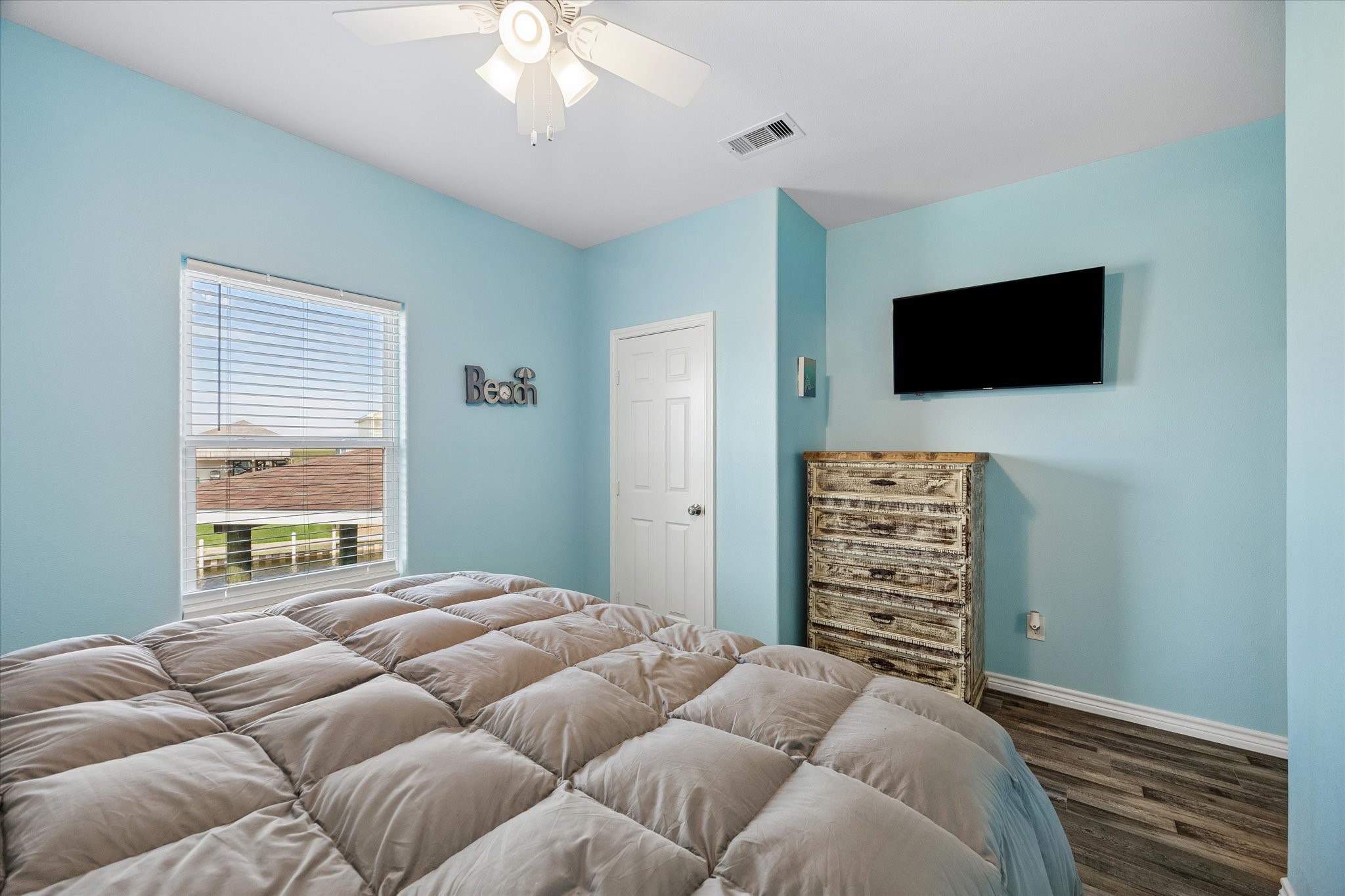 Cozy bedroom with soft blue walls, featuring a ceiling fan, complemented by a large window for natural light.