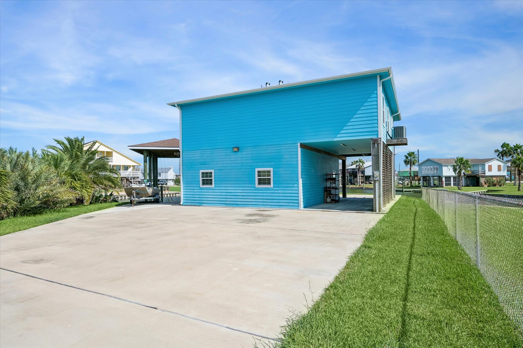 Experience coastal living in this spacious retreat, featuring vibrant blue siding, an expansive driveway, and a versatile open-air covered area perfect for soaking in the outdoors.