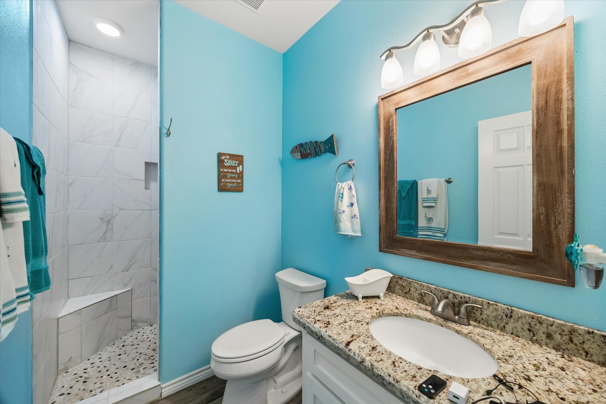 Bright and inviting bathroom with a coastal vibe, featuring a spacious walk-in shower with marble tile, granite countertop, and stylish fixtures.
