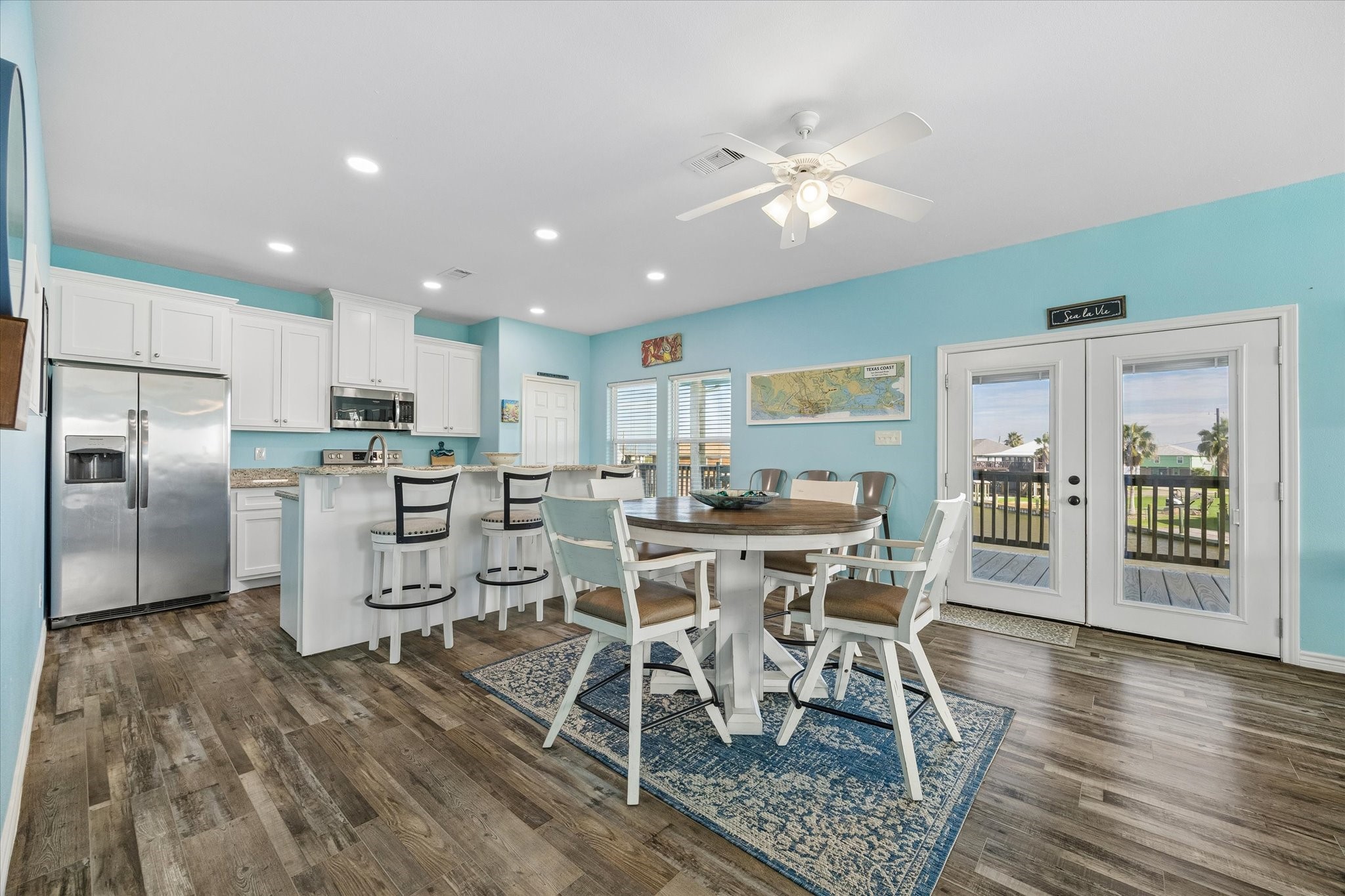 Experience the perfect blend of style and functionality in this bright and airy kitchen-dining area, featuring white cabinetry, a sleek stainless steel fridge, and a central island, all enhanced by modern lighting, cheerful blue walls, and French doors leading to scenic outdoor views. Experience the perfect blend of style and functionality in this bright and airy kitchen-dining area, featuring white cabinetry, a sleek stainless steel fridge, and a central island, all enhanced by modern lighting, cheerful blue walls, and French doors leading to scenic outdoor views.
