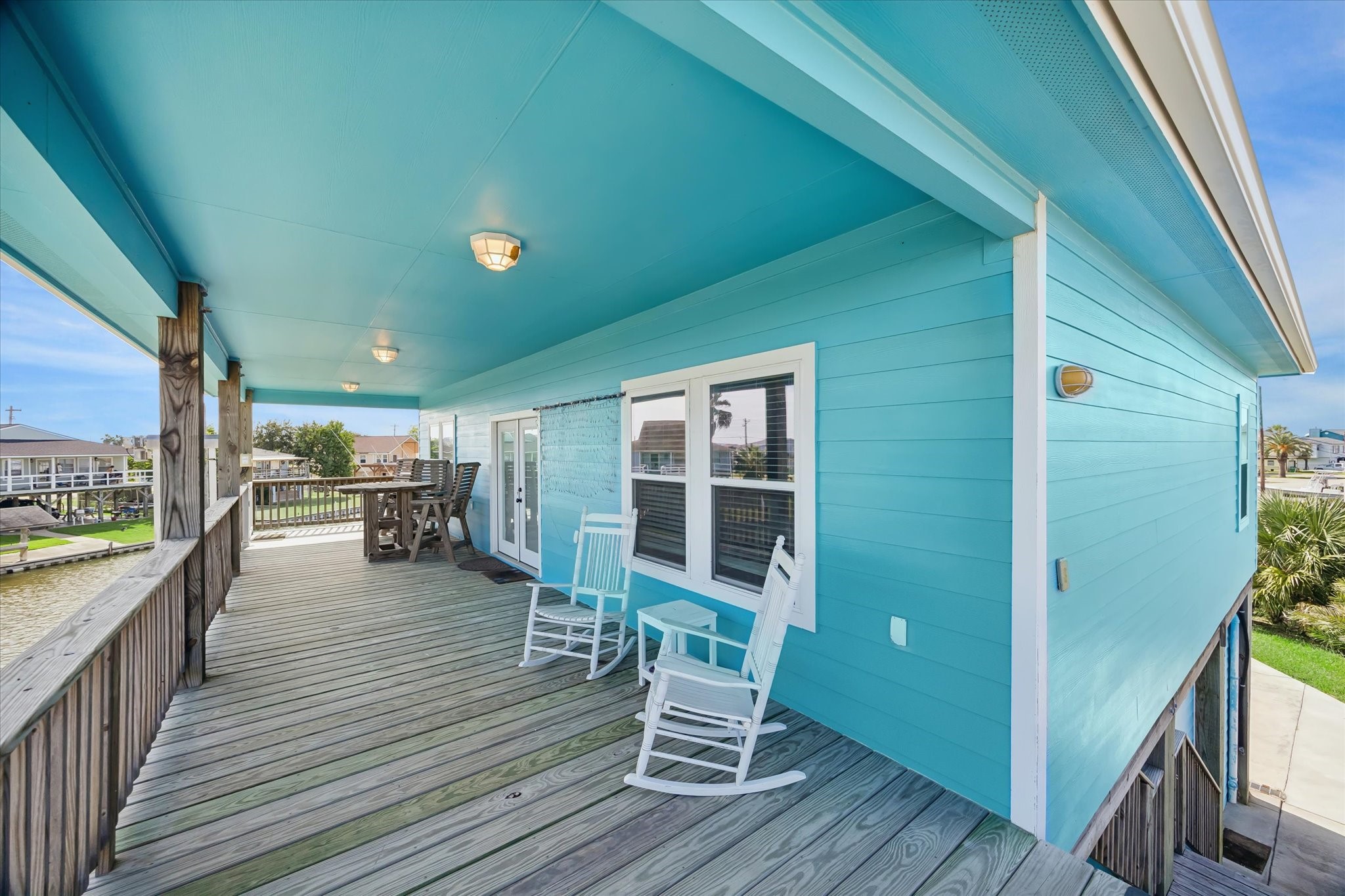 Charming coastal retreat with vibrant turquoise siding and a spacious wooden deck, perfect for relaxing in rocking chairs and enjoying outdoor dining.