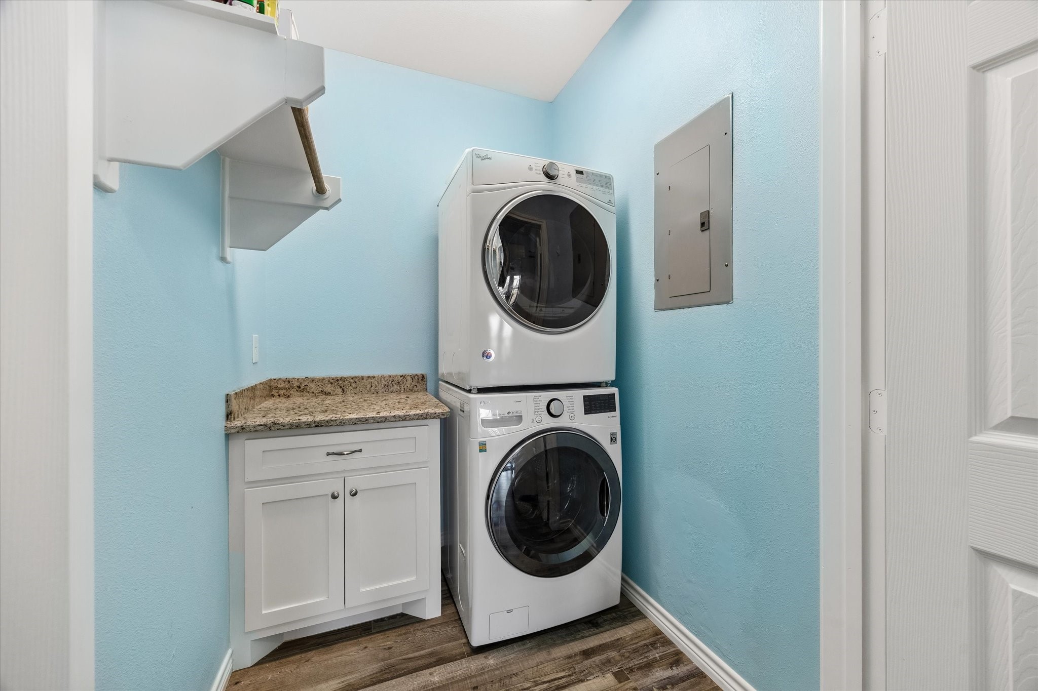 Bright and efficient laundry room featuring a stacked washer and dryer, sleek granite countertop, and ample storage with a modern cabinet and shelving.