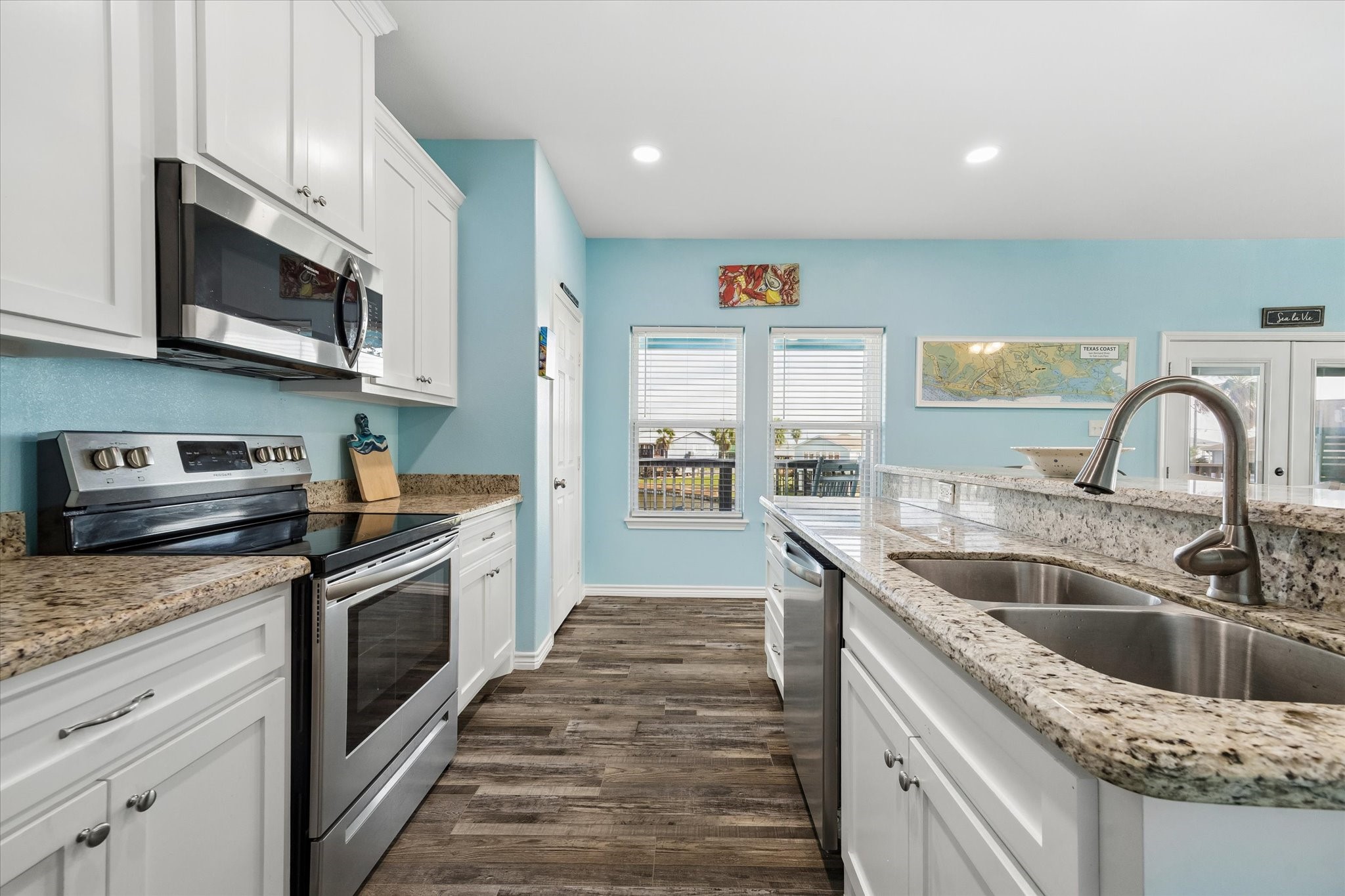 Bright and inviting kitchen featuring granite countertops, stainless steel appliances, and charming wood-look flooring, all complemented by soothing blue walls and ample natural light. Bright and inviting kitchen featuring granite countertops, stainless steel appliances, and charming wood-look flooring, all complemented by soothing blue walls and ample natural light.