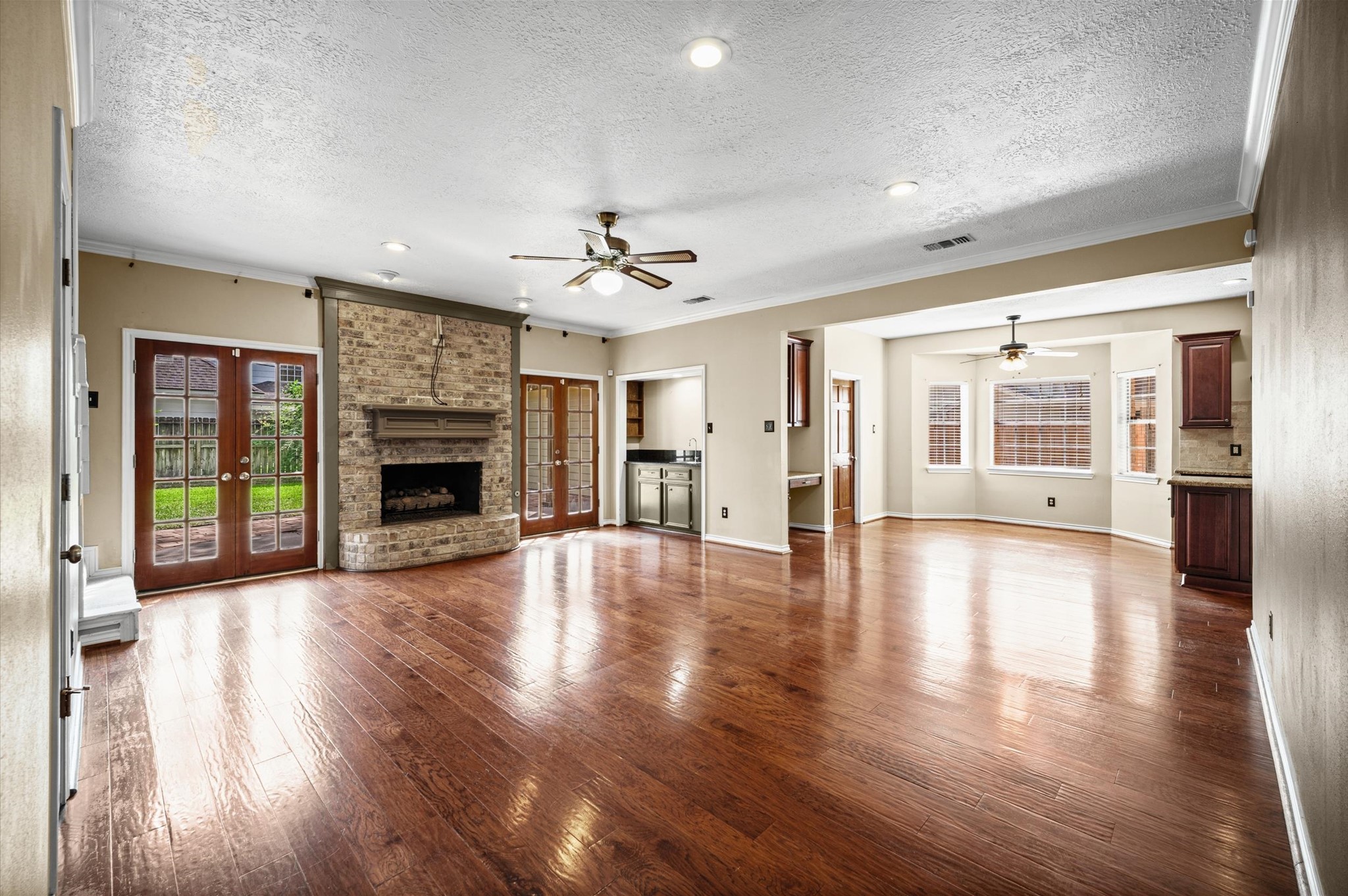 Spacious living room with beautiful brick fireplace, two sets of french doors, wood floors and a wet bar- perfect for gathering and entertaining.