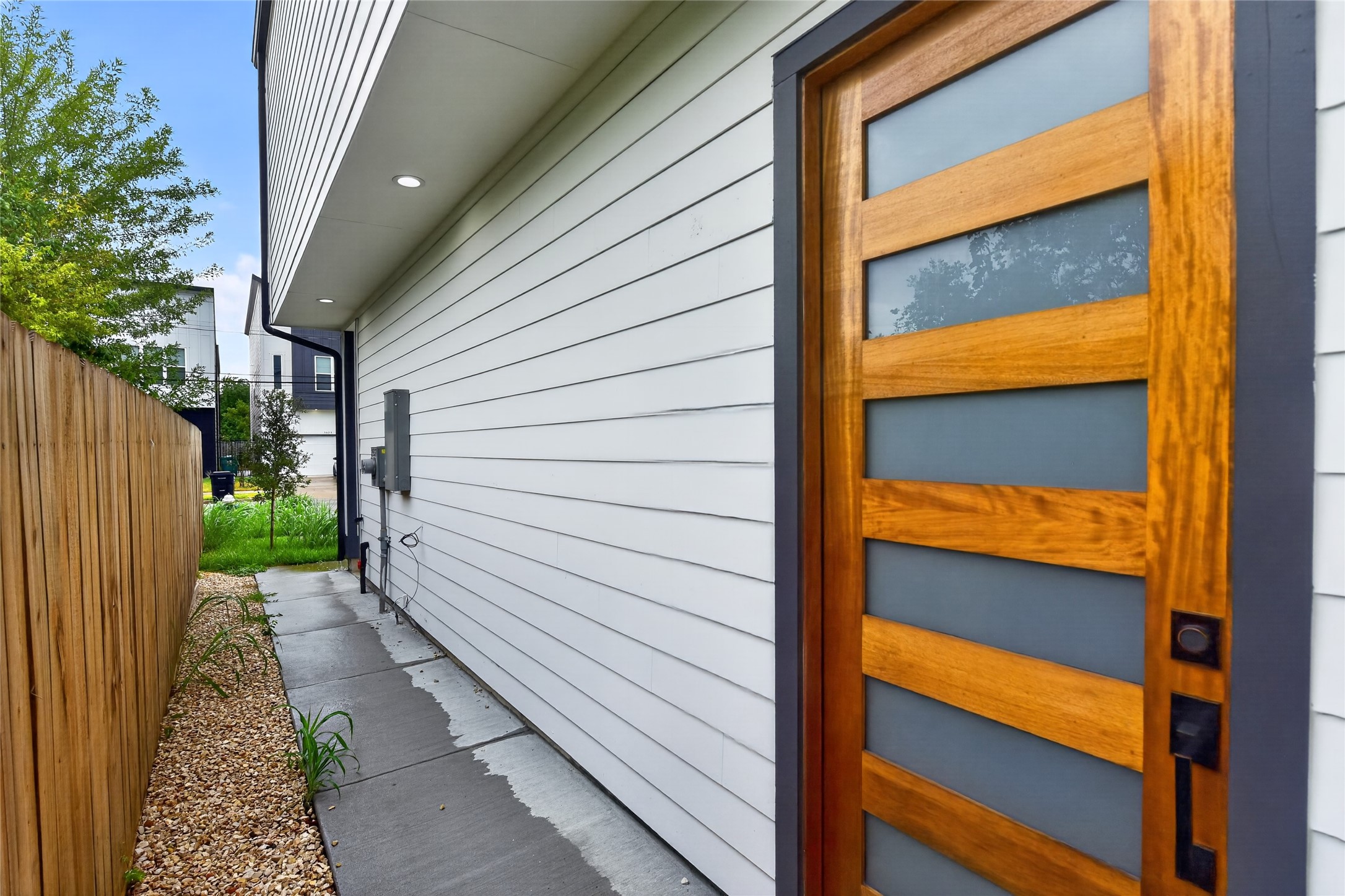 A clean well-lit concrete walkway leads to the contemporary front door, opening into bright, living spaces that flow naturally through to the backyard.