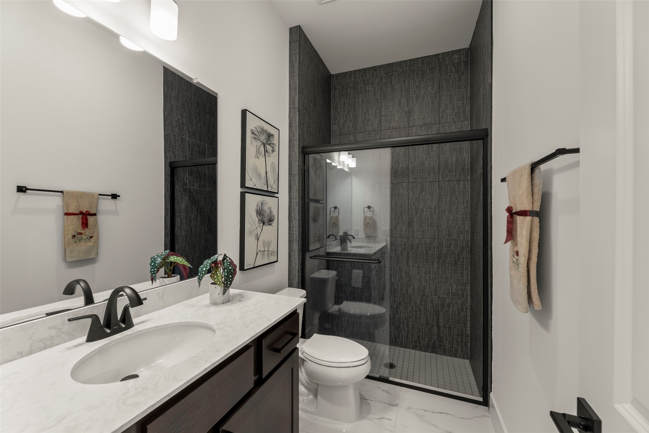 Elegant bathroom featuring a sleek glass-enclosed shower, modern fixtures, and a marble countertop, accented by stylish decor and artwork.