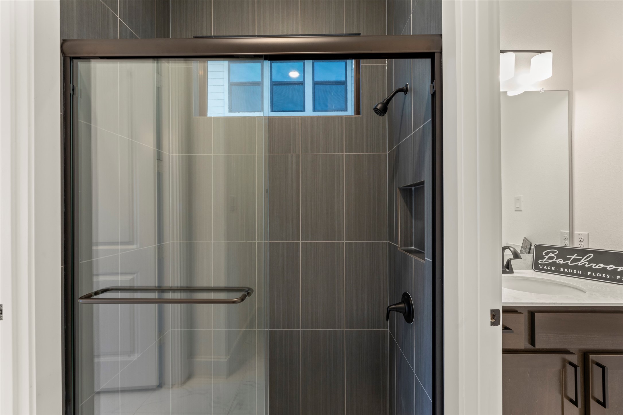 Glass-enclosed shower with sleek dark tiles and a convenient built-in niche.