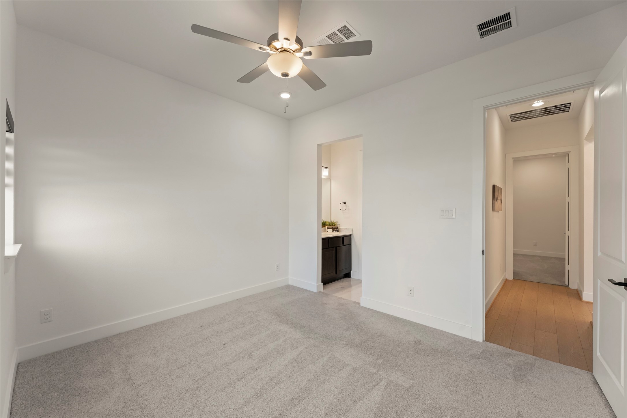 Ensuite bathroom and access to a hallway with elegant wood flooring.