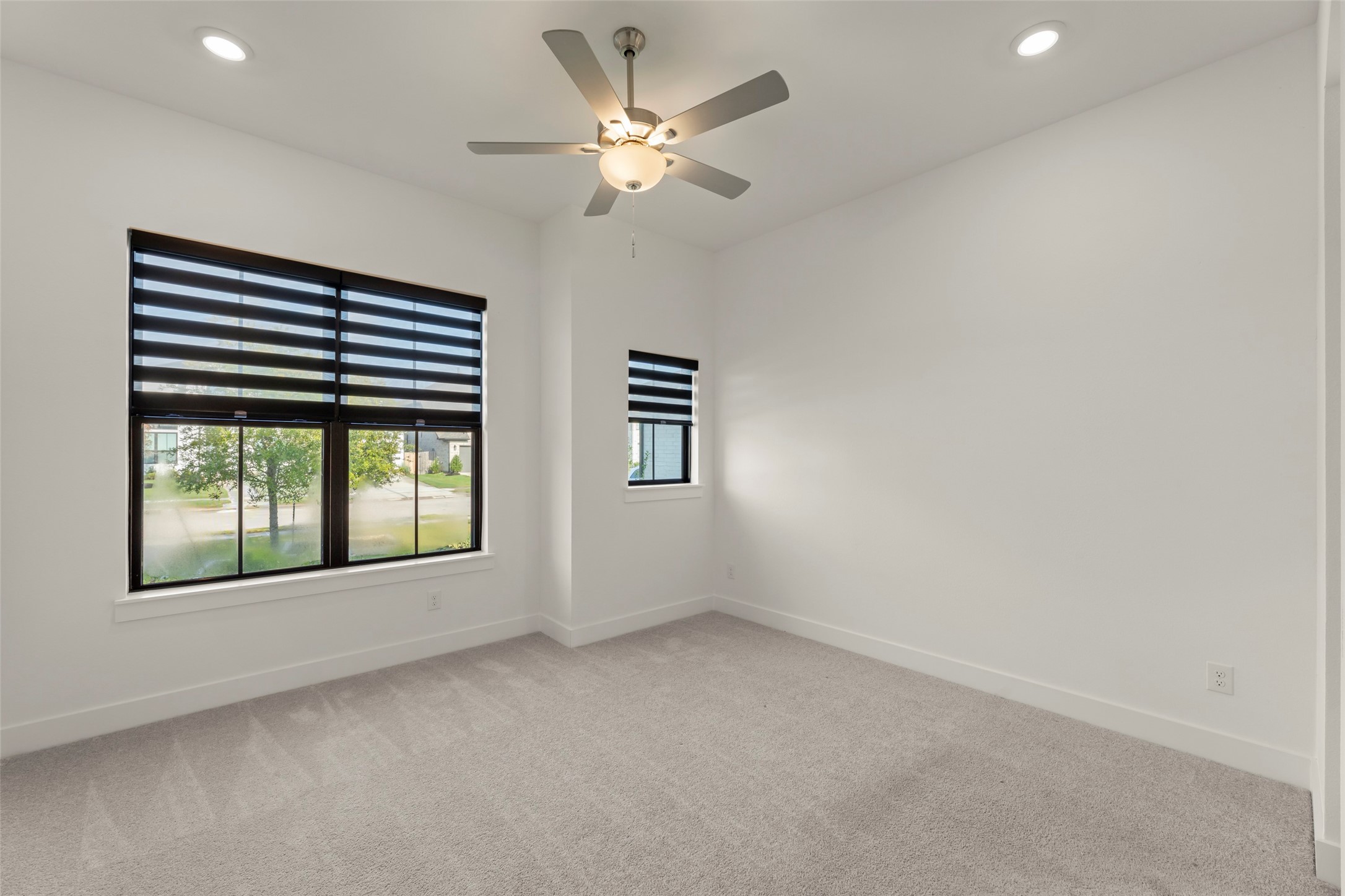 Vibrant room with large windows, modern blinds, plush carpeting, and a ceiling fan for comfort.
