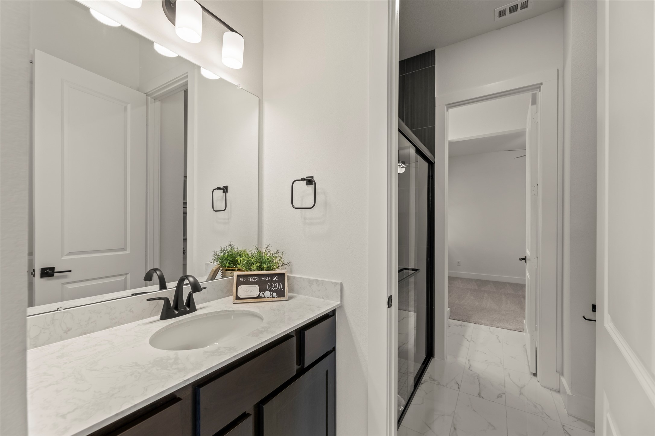 Lovely bathroom featuring a modern vanity with a sleek marble countertop and dark cabinetry, complemented by contemporary lighting and a spacious shower with glass doors.