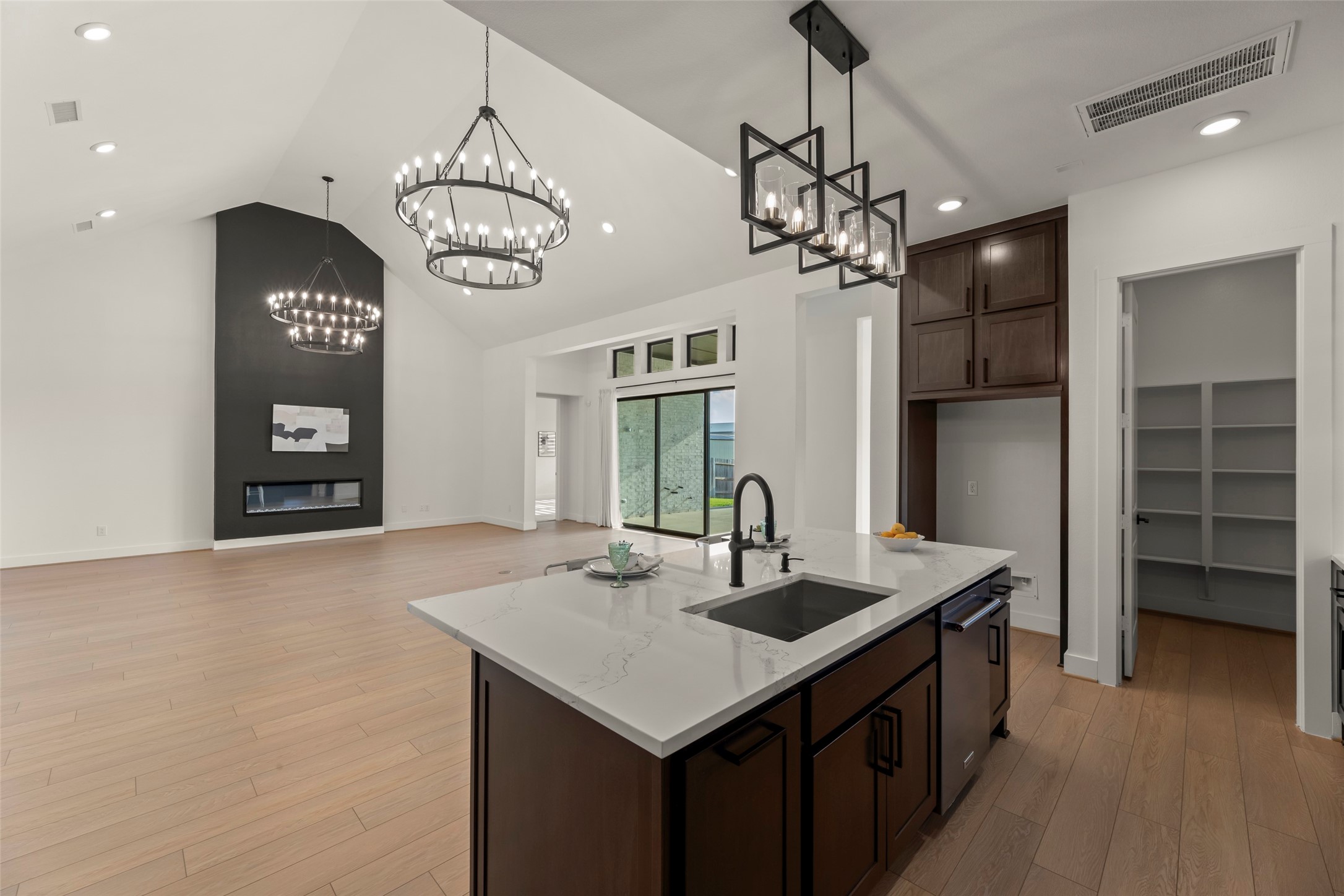 High ceilings, modern chandeliers, and a sleek fireplace. The kitchen features a large island with a marble countertop and ample storage space, seamlessly connecting to the living space.