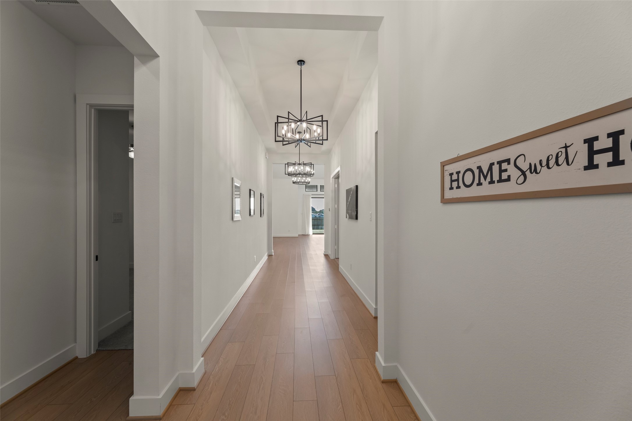 Lit entryway with modern light fixtures and warm wood flooring leads to the heart of the home.
