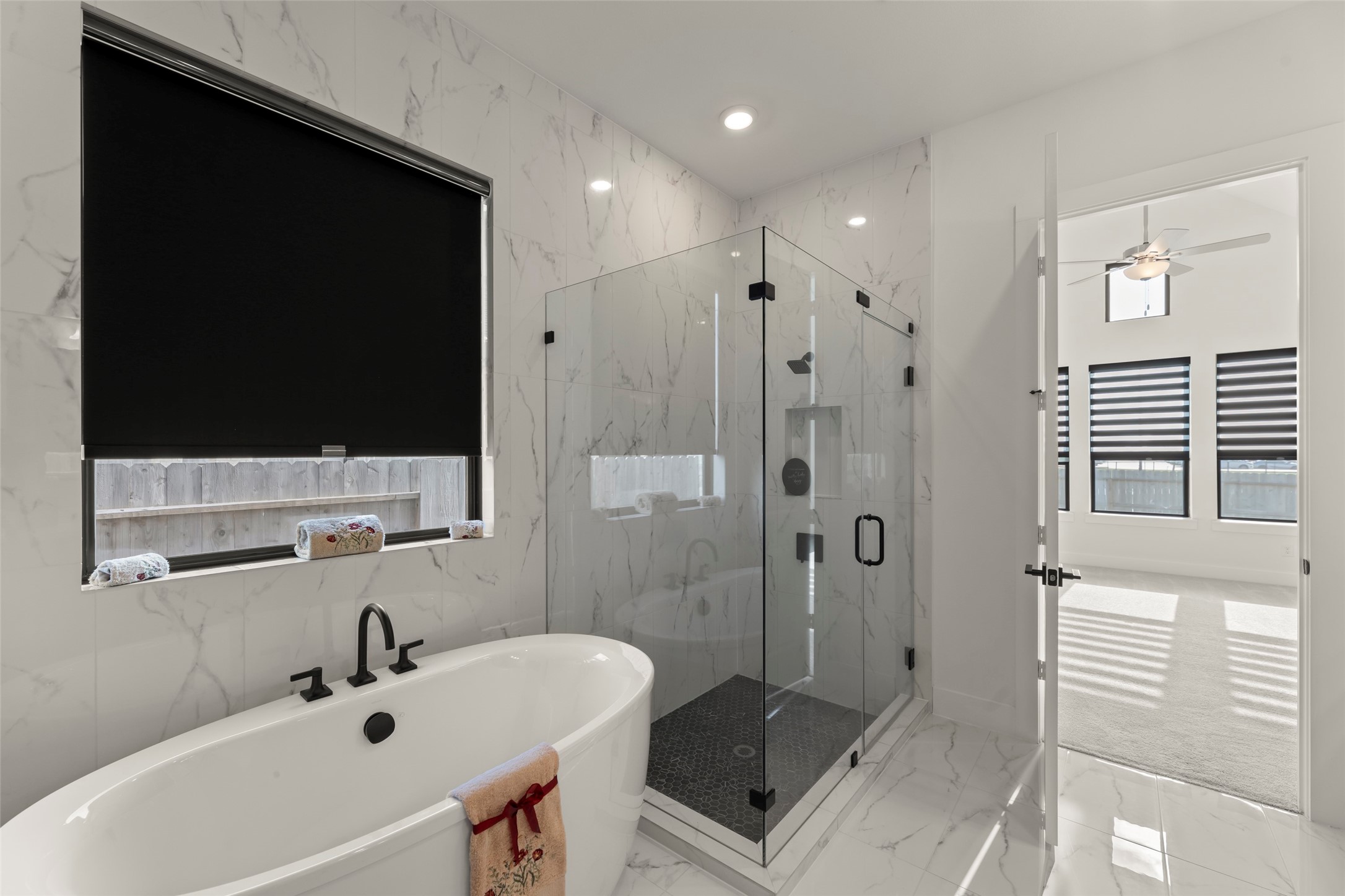 Freestanding tub and a spacious glass-enclosed shower, enhanced by elegant marble-patterned walls and floors.