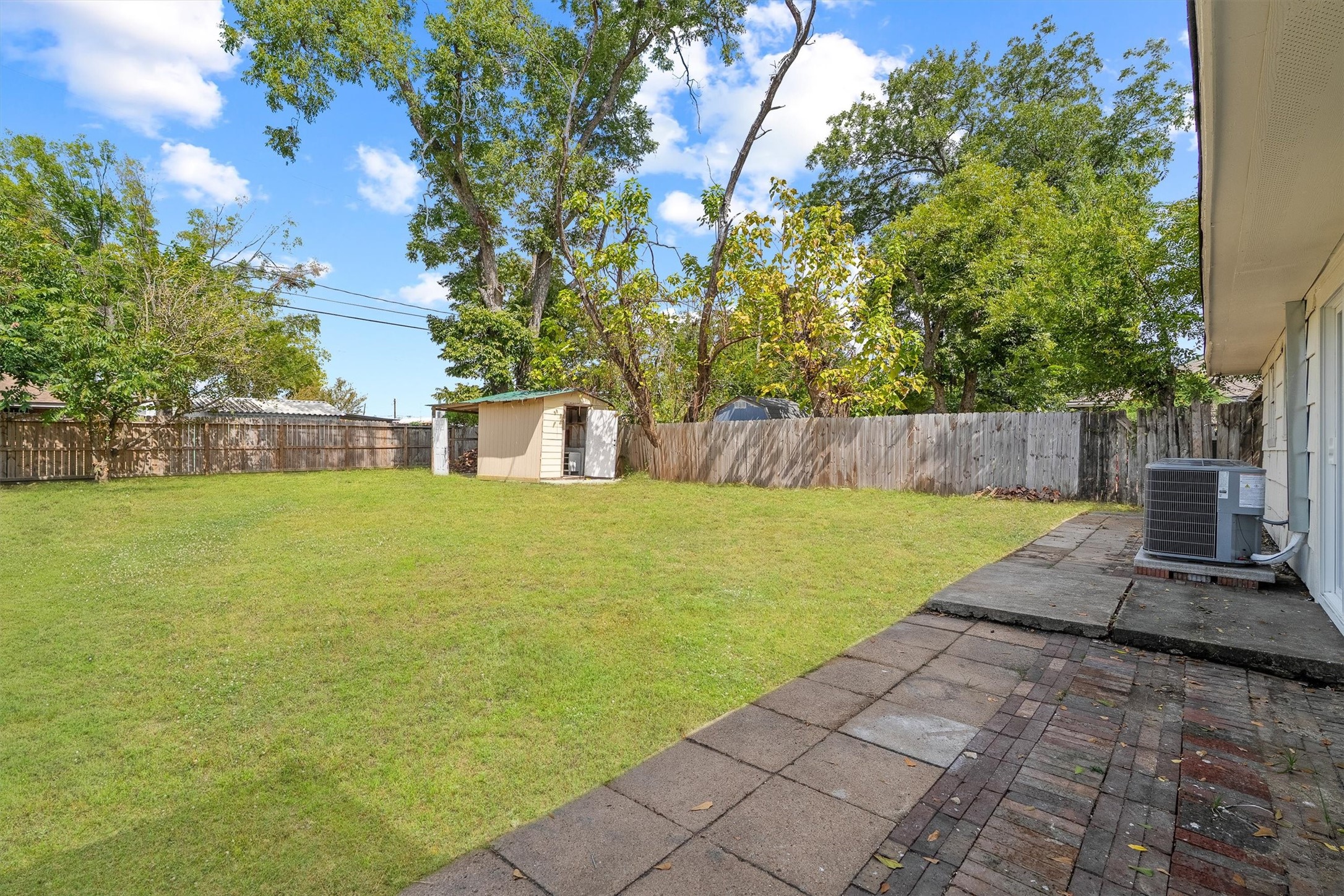 Spacious backyard with a well-maintained lawn, a convenient storage shed, and a paved patio area perfect for outdoor activities and relaxation.