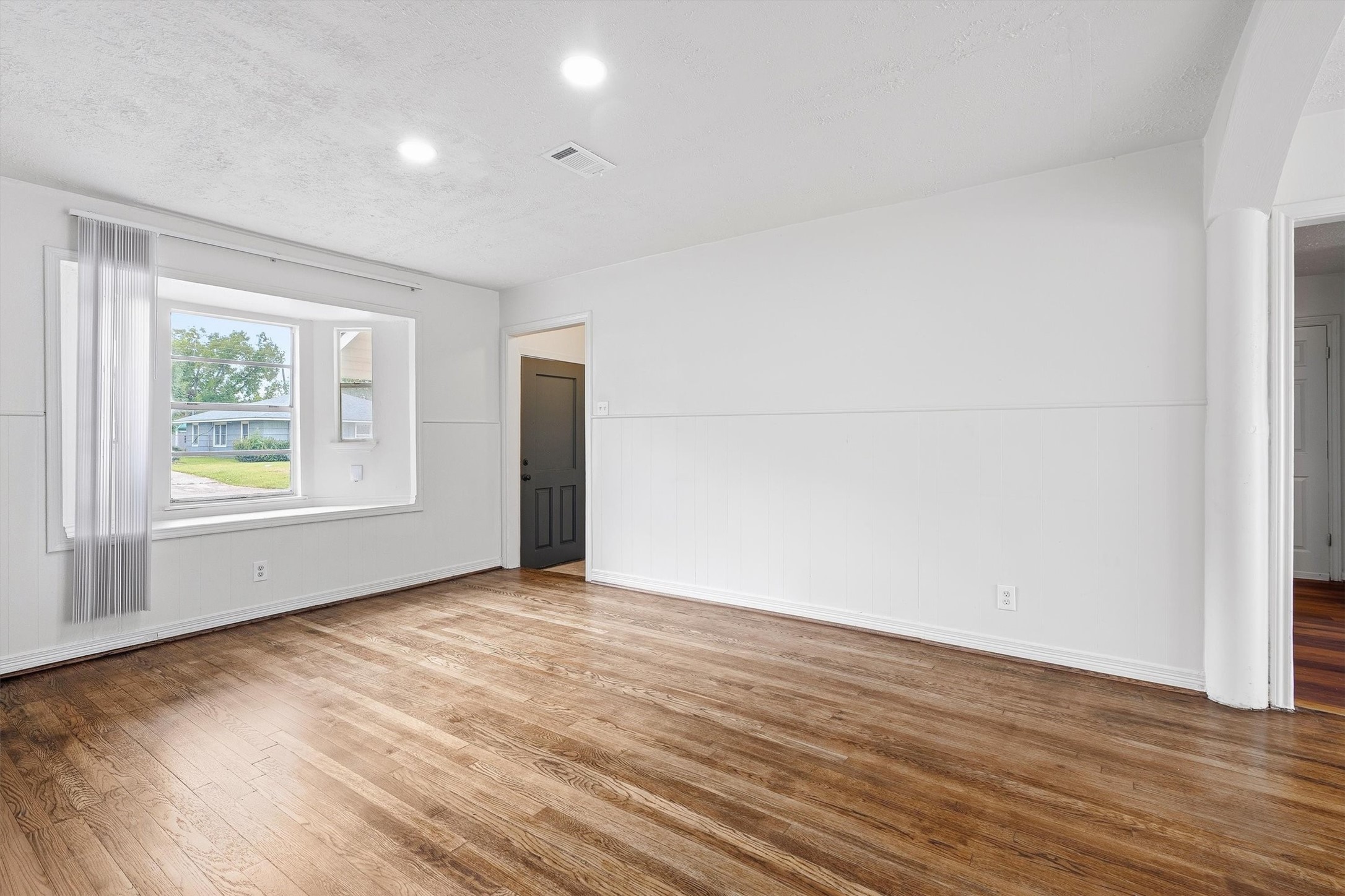Bright and inviting living space featuring hardwood floors, fresh white walls, and a charming bay window that offers plenty of natural light.