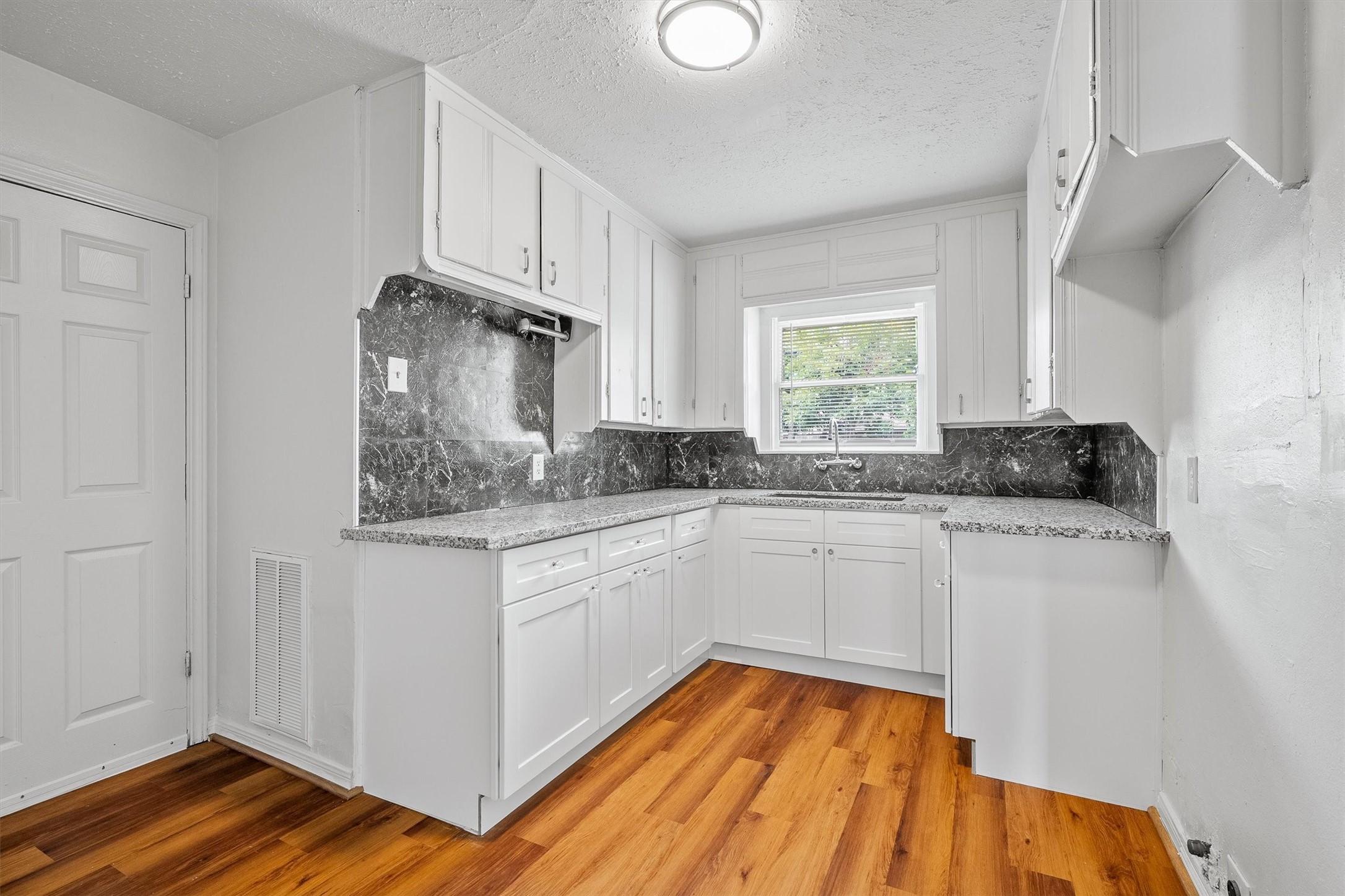 Bright kitchen featuring sleek white cabinetry, elegant dark countertops, and warm wood flooring, offering a charming and functional space.