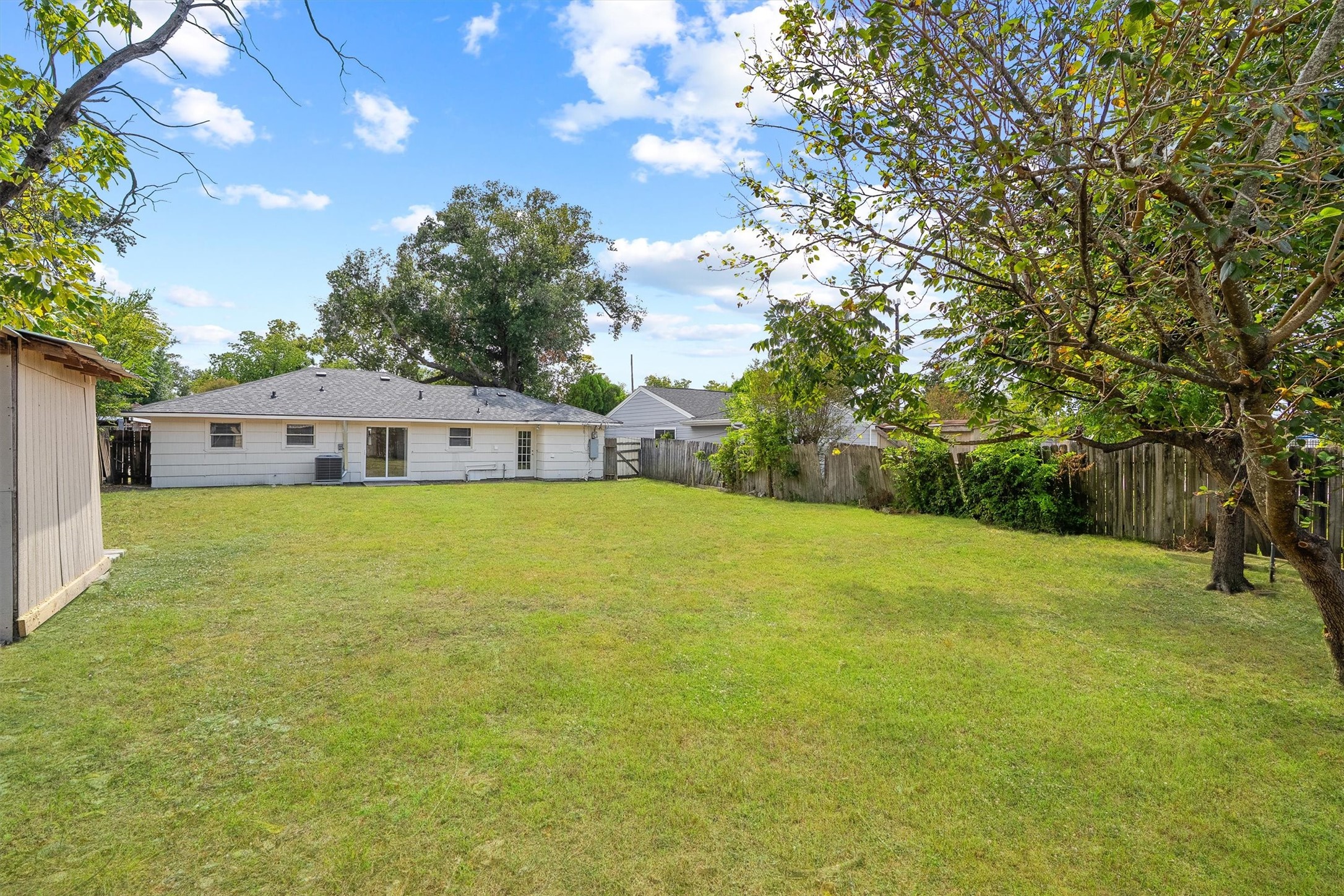 Expansive backyard with lush greenery, perfect for outdoor activities and entertainment, featuring a charming single-story home and mature trees offering ample shade.