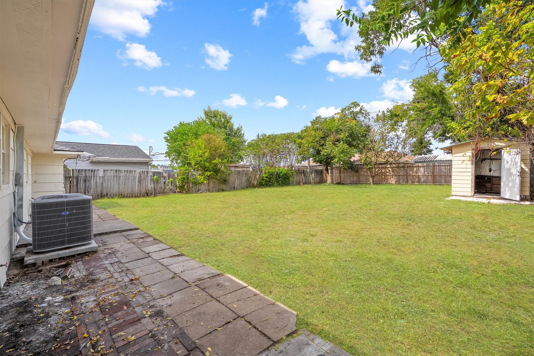Expansive backyard with lush green grass, a spacious patio area, and a convenient storage shed, perfect for outdoor activities and gatherings.