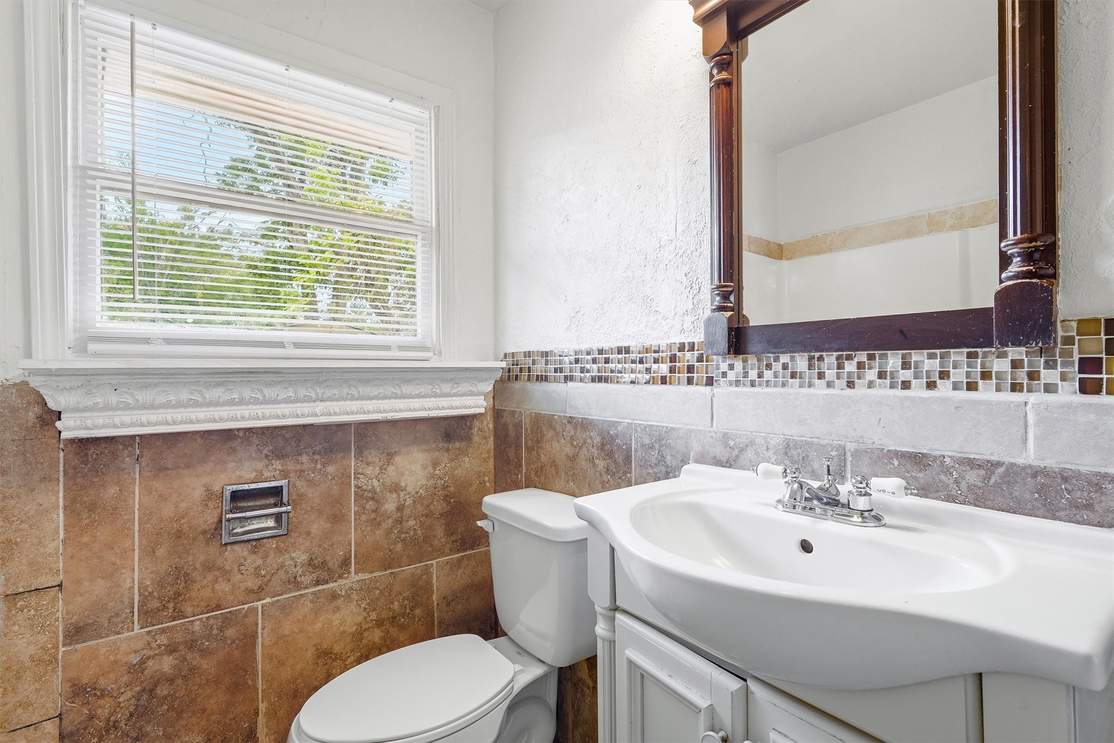 Charming bathroom featuring elegant tile work, a classic vanity with a decorative mirror, and a bright window that fills the space with natural light.