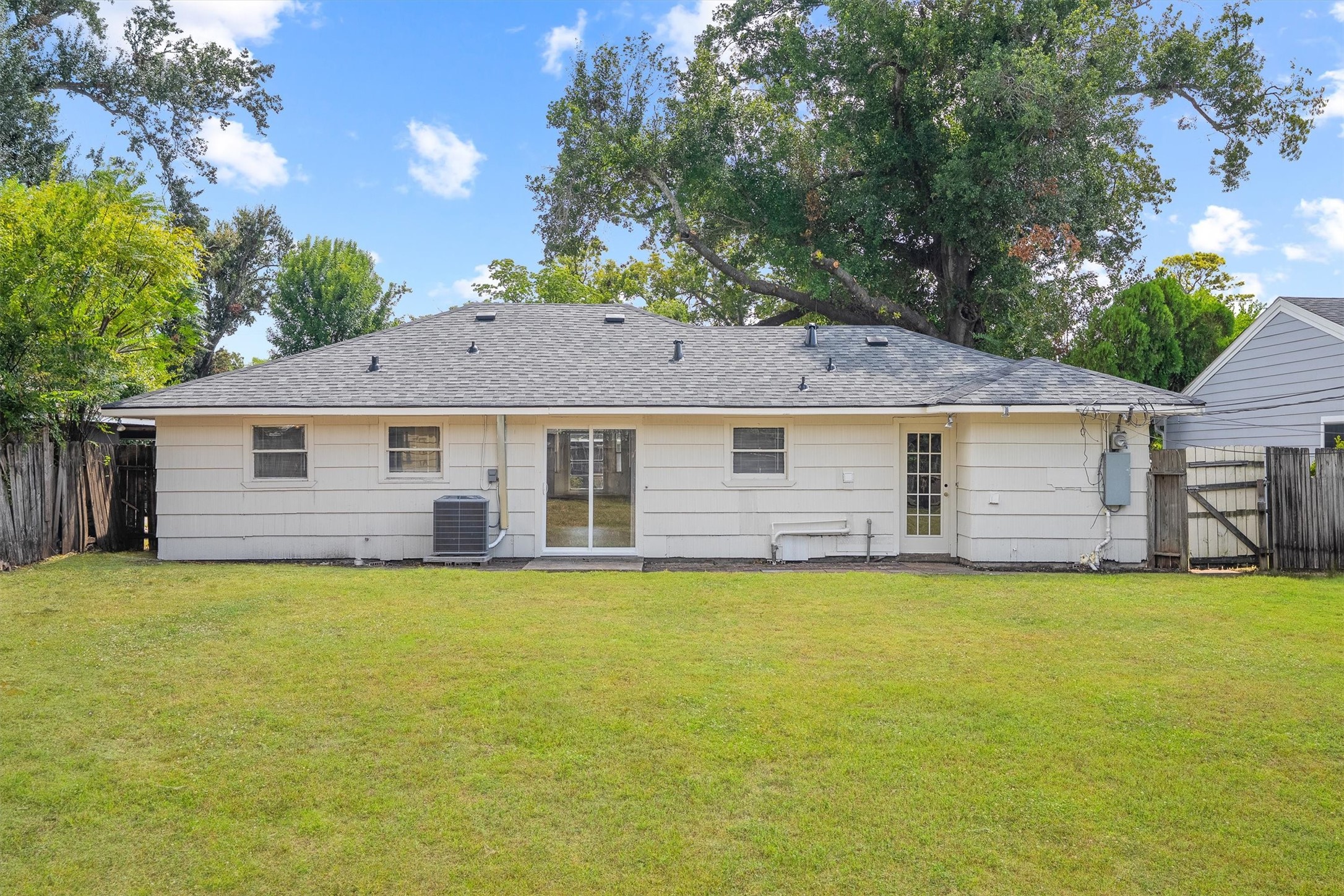 Charming single-story home with a spacious backyard, perfect for outdoor activities. The exterior features a sturdy roof and convenient patio access, surrounded by mature trees for added privacy.