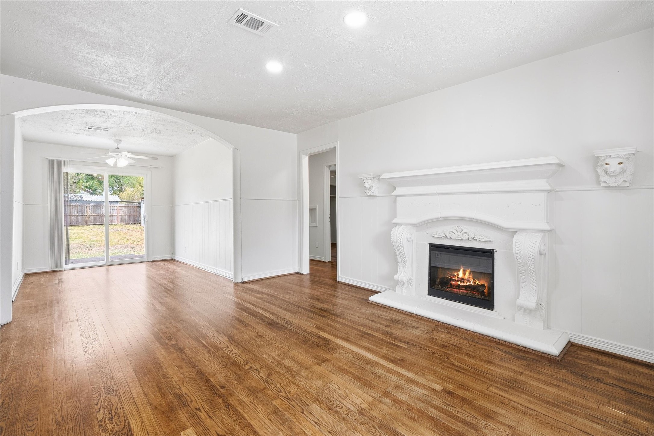Elegant living space featuring a stunning white fireplace, rich hardwood floors, and ample natural light streaming through sliding glass doors leading to the backyard.