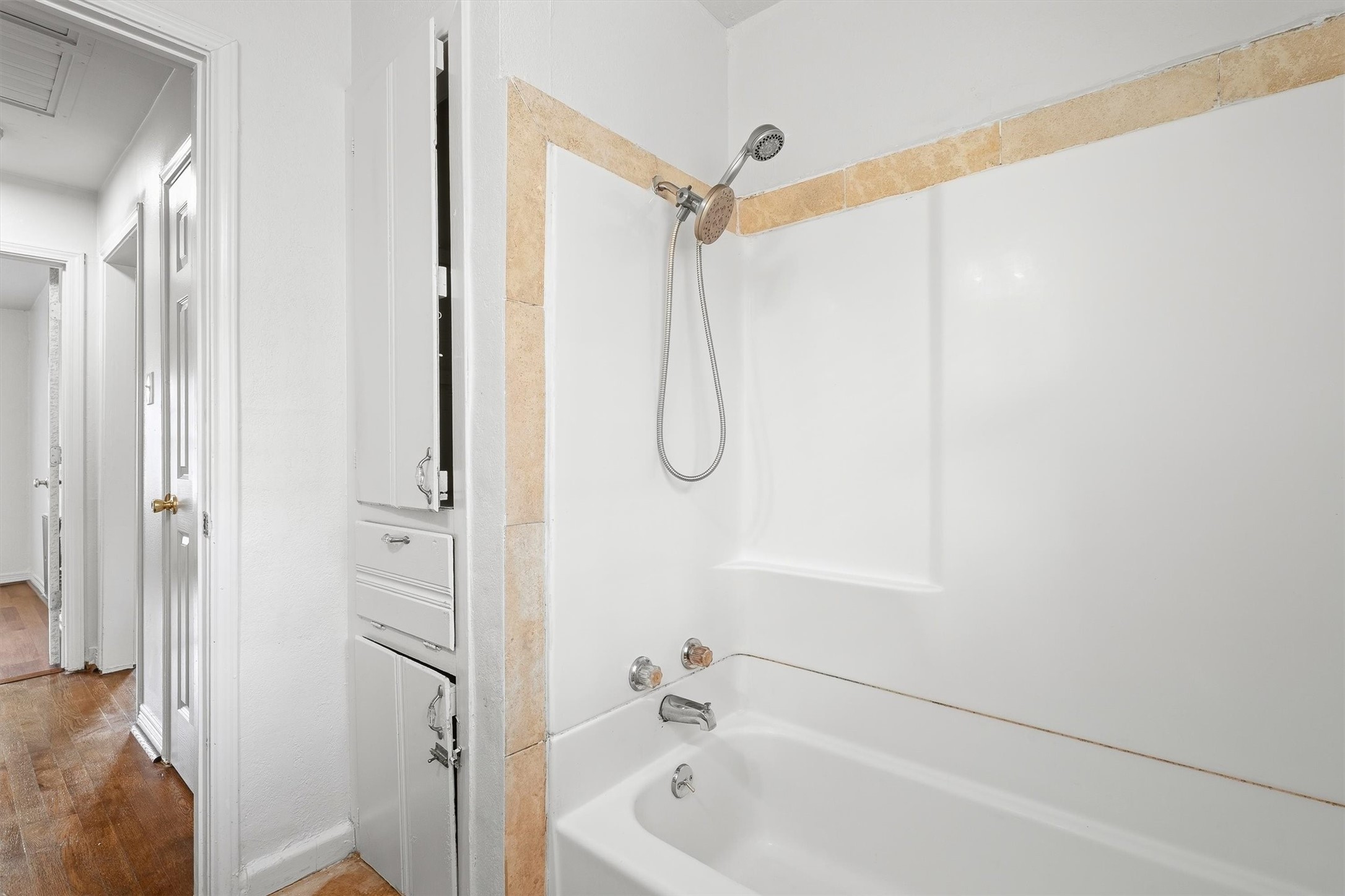 Bright and clean bathroom featuring a classic bathtub with shower, accented by tasteful tiling and convenient built-in storage.