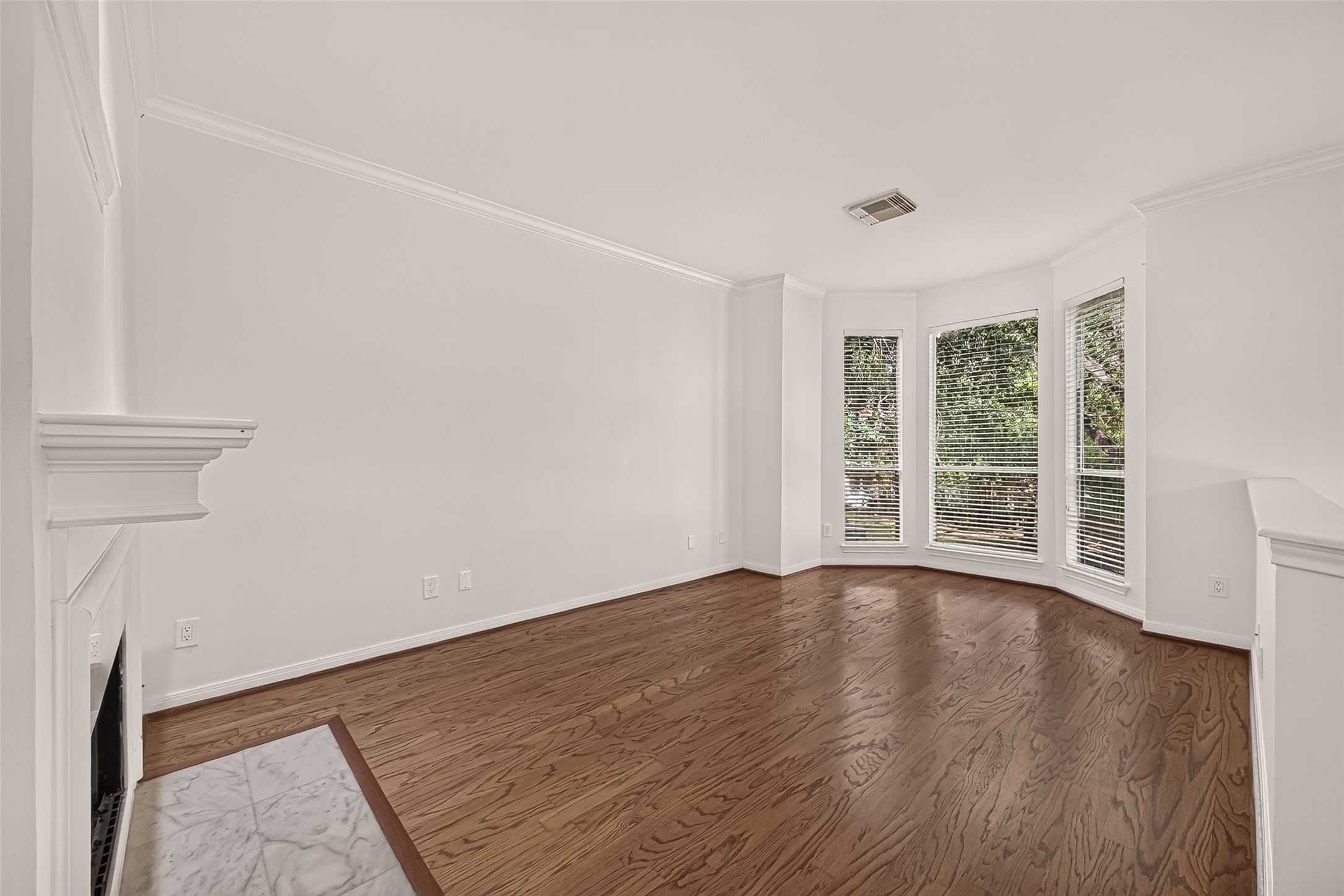 The second-floor living room offers a welcoming place to relax, featuring bay windows, warm wood flooring, and a beautifully updated fireplace with a new marble surround.