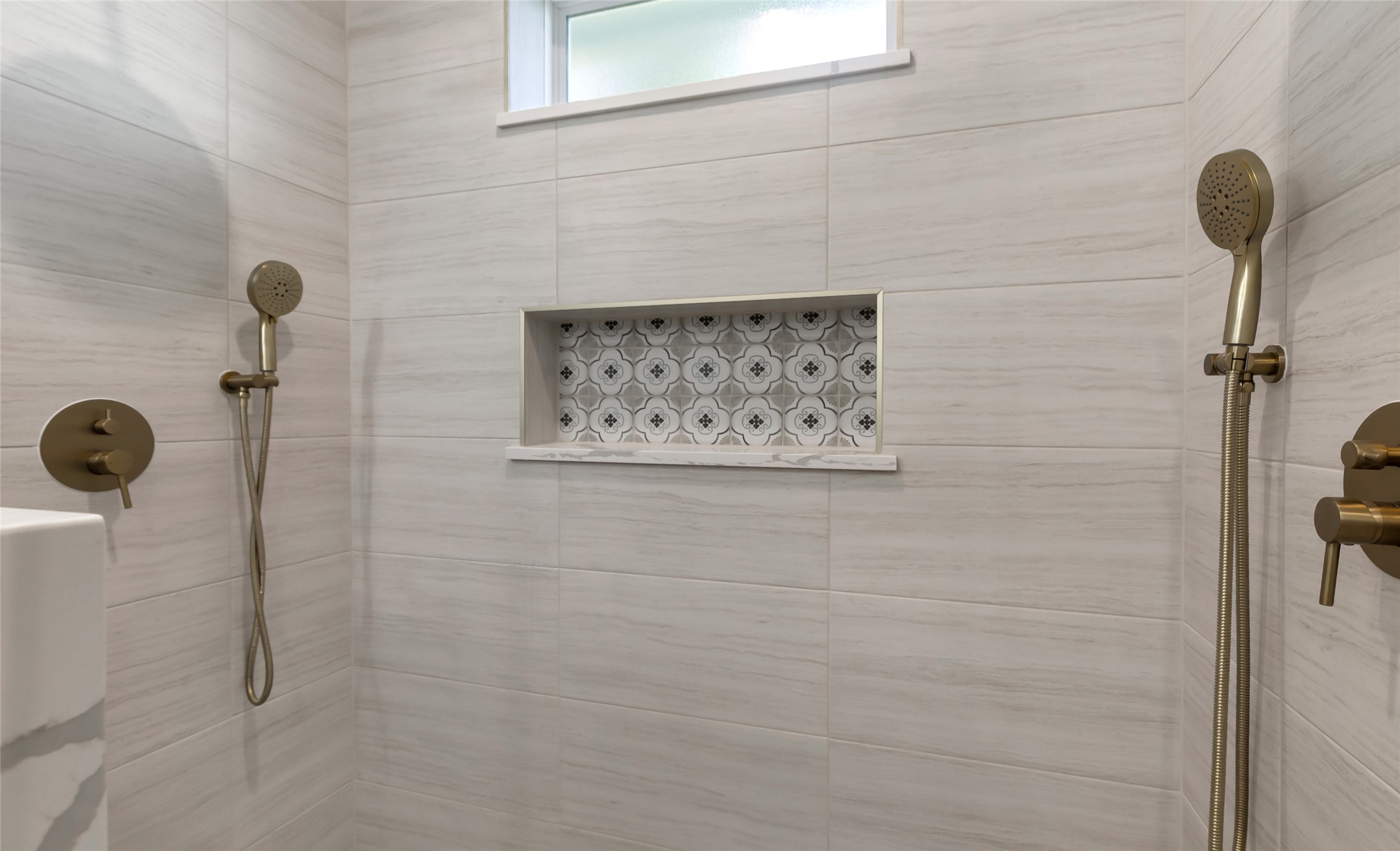 Primary shower, featuring elegant dual showerheads, chic modern tiling, and a stylish recessed shelf for added convenience.