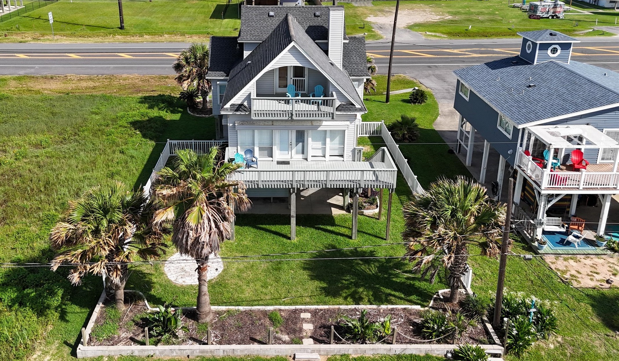 This attractive coastal home features a raised design with a spacious front deck and balcony, perfect for enjoying ocean views. Surrounded by lush greenery and palm trees, it offers a relaxed beachside atmosphere. The house is conveniently located with easy access.