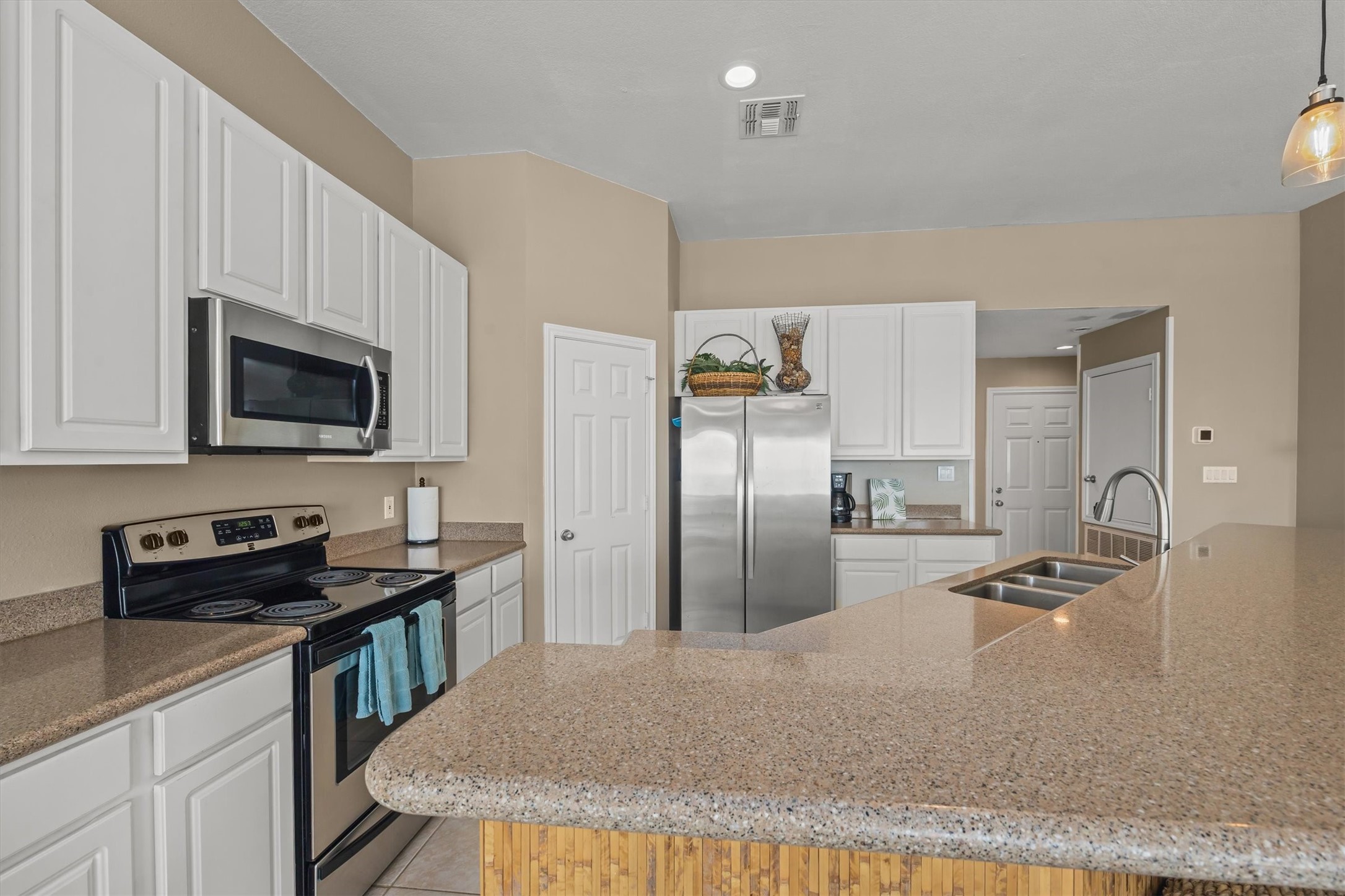 The modern kitchen features ample counter space with stainless steel appliances, white cabinetry, and a spacious island with a double sink. The layout offers a clean and functional design, ideal for cooking and entertaining.