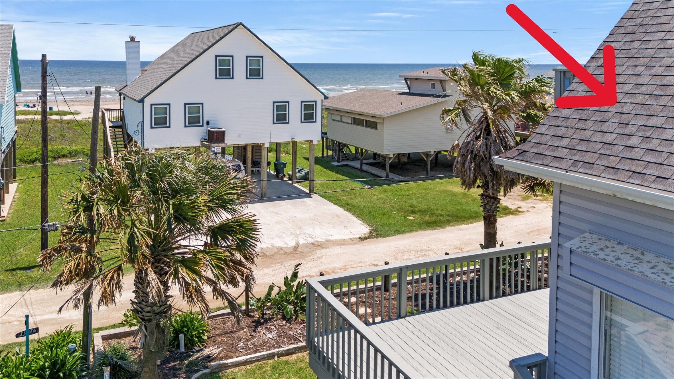 The spacious deck provides great ocean views, surrounded by palm trees. The elevated design offers direct access to a sandy road leading to the beach. Ideal for enjoying seaside living.