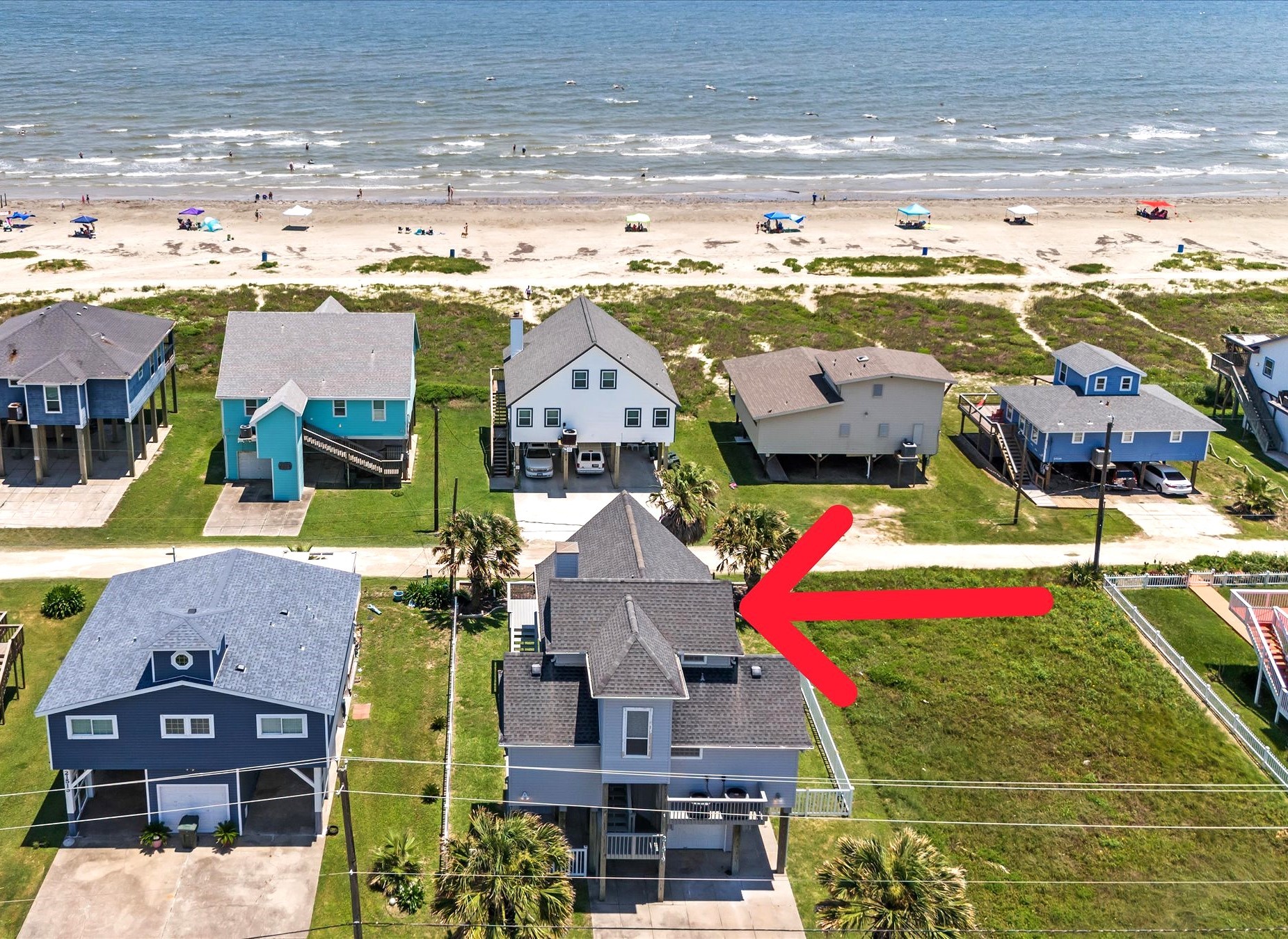 This photo shows this beachside home with a prime location just steps from the ocean. The house features elevated construction for the best views.  An arrow highlights this specific home for sale.