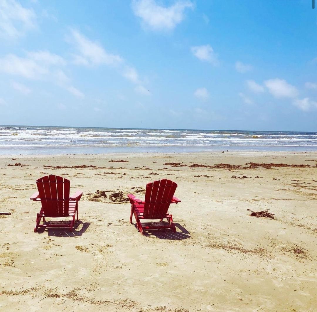 This photo features a serene beach scene with two red Adirondack chairs facing the ocean, perfect for enjoying seaside views and relaxation in a coastal home setting.