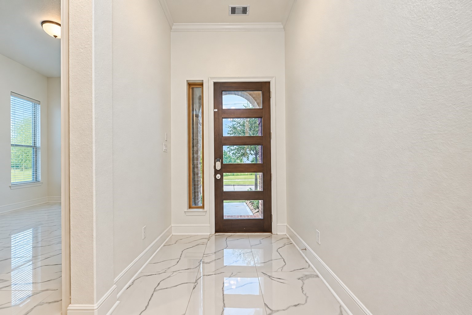 A welcoming entryway featuring a striking modern front door with glass panel inserts, elegant marble-like tile flooring, and crisp neutral walls, creating a bright, sophisticated first impression with timeless appeal