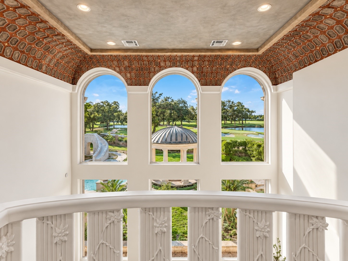 Beautiful arched windows frame sweeping views of the landscaped grounds and golf course setting, bringing natural light and scenic surroundings into the upper levels of the estate.