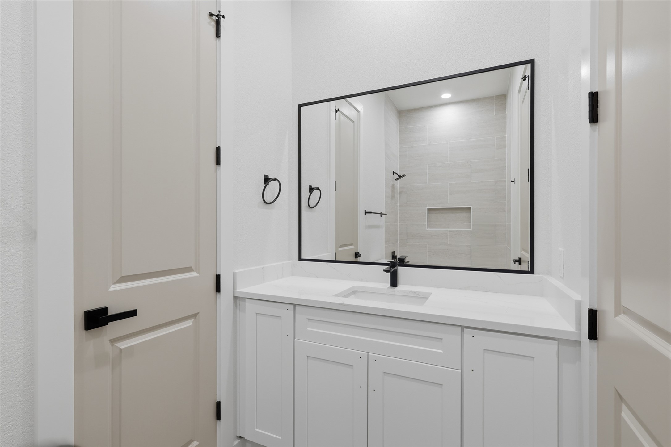 Elegant bathroom featuring a sleek white vanity with a modern black-framed mirror, complemented by a spacious tiled shower area with a built-in shelf.