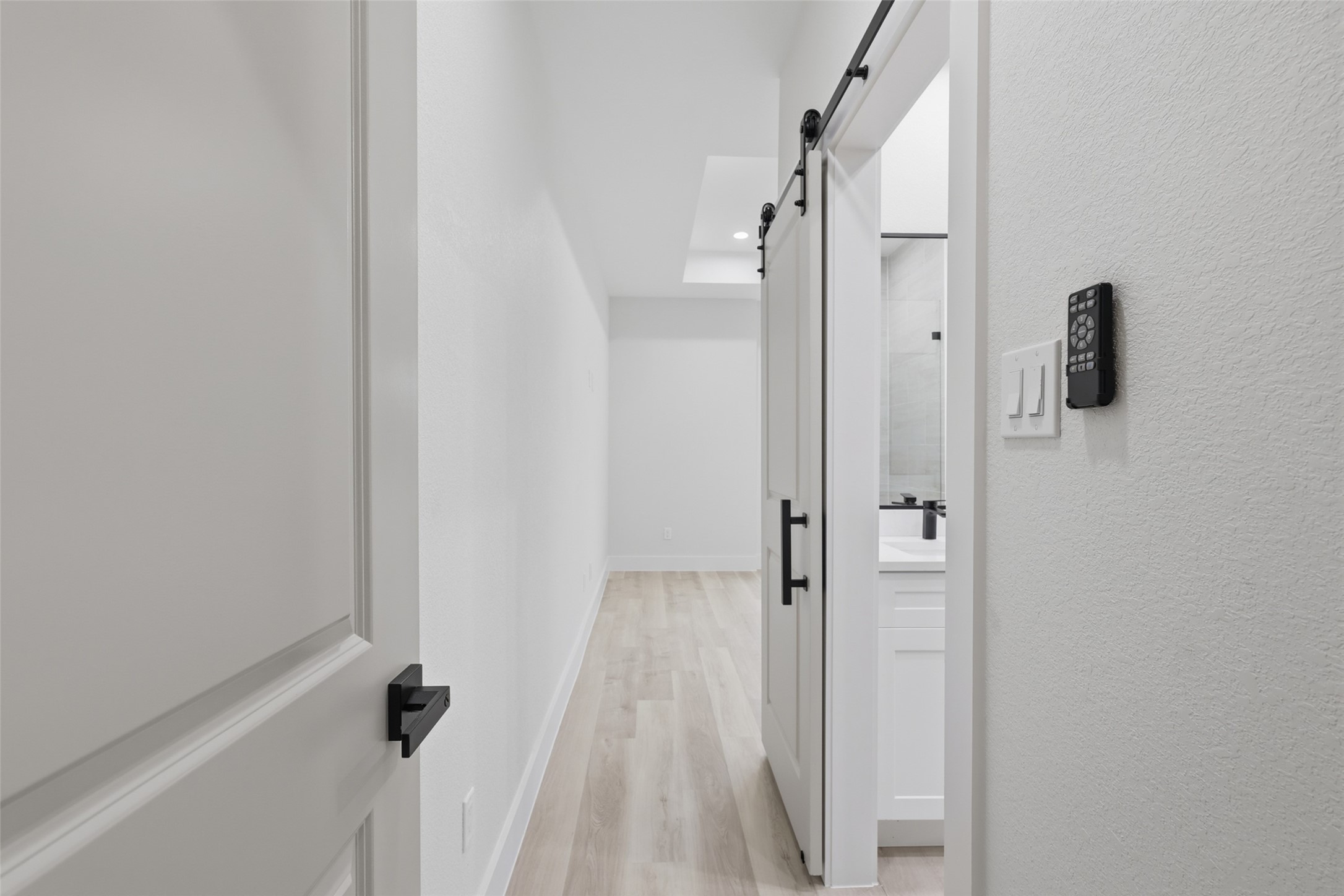 Modern hallway with sleek, light wood like flooring for the primary bedroom (upstairs) leading to a space with a stylish sliding barn door to the private bathroom, creating a contemporary and inviting atmosphere.