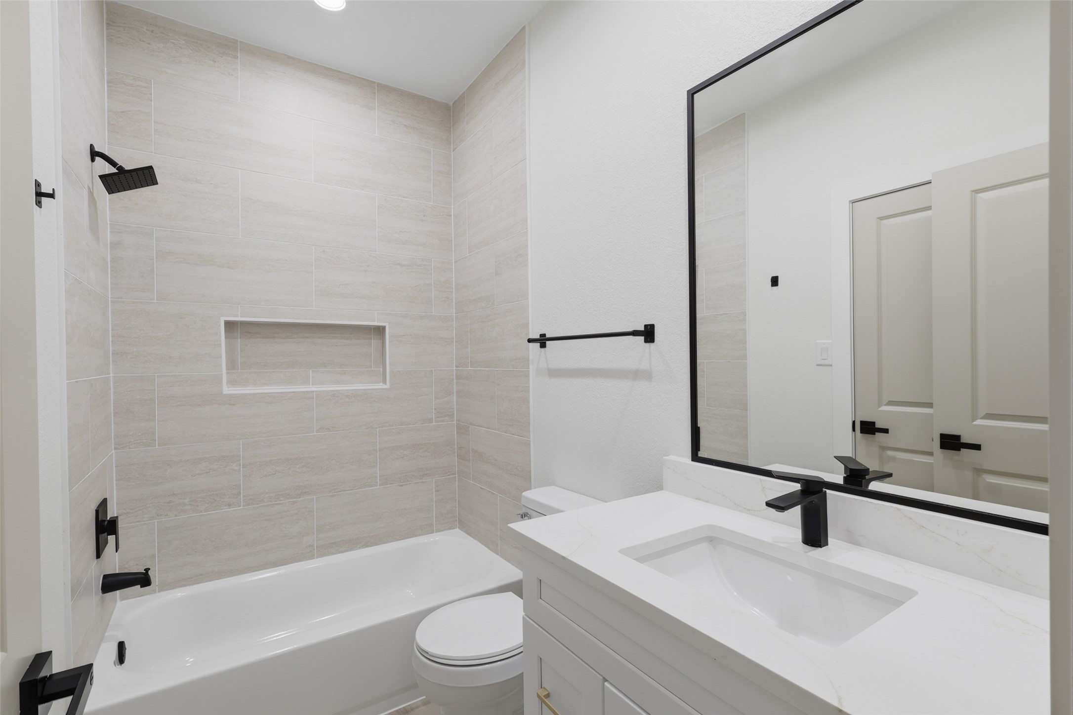 Modern bathroom featuring sleek black fixtures, a spacious vanity with a large mirror, and a stylish tiled shower-tub combo.