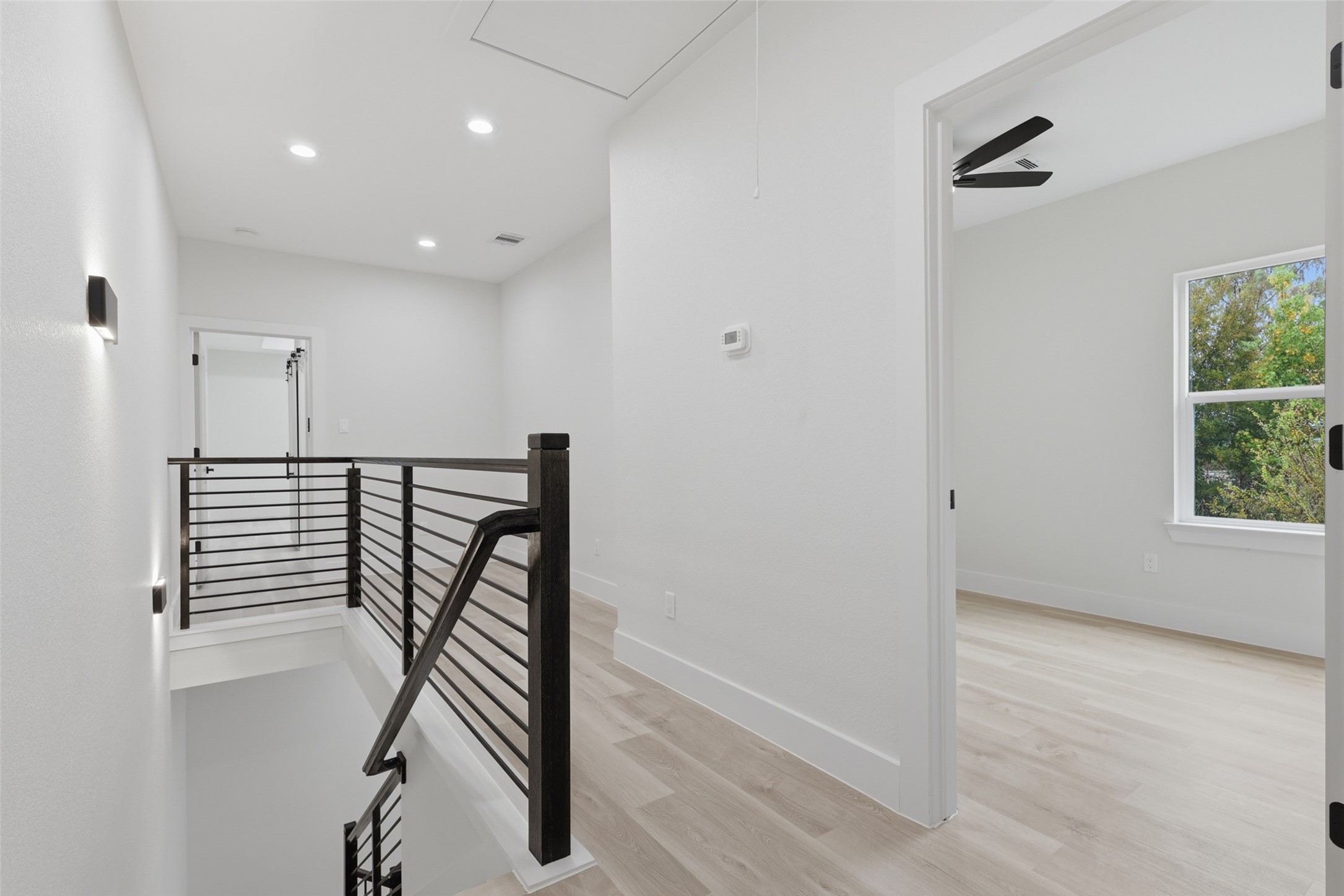 Bright and modern upstairs landing with sleek railings, recessed lighting, and access to a sunlit room, creating a welcoming and open atmosphere.