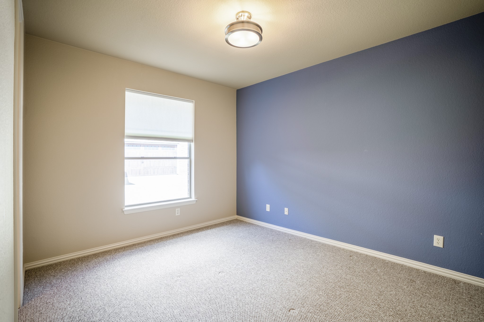Returning to the front of the home, this secondary bedroom suite sits near the office/study and offers a quieter transition from the main living areas. The window brings in natural light, while the blue accent wall adds contrast and gives the room a defined, finished feel before the walkthrough continues into the nearby bath.