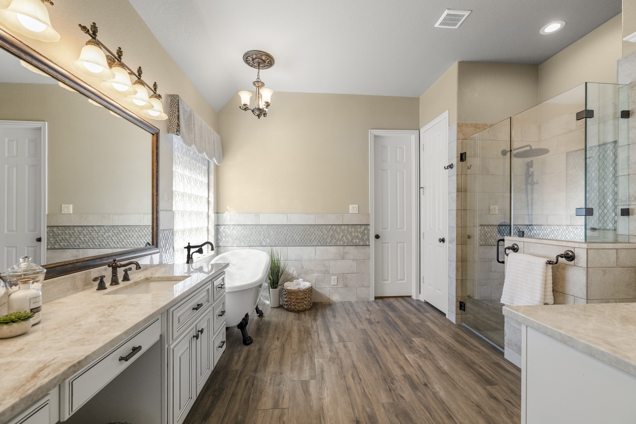 Continuing into the remodeled primary bath, the suites upgraded finish comes into focus with Taj Mahal quartzite, Emser tile, dual vanities, a freestanding clawfoot tub, and a glass-enclosed shower. The door straight ahead leads into the walk-in closet, keeping the bath and closet connected in a way that feels polished, private, and easy to live in.