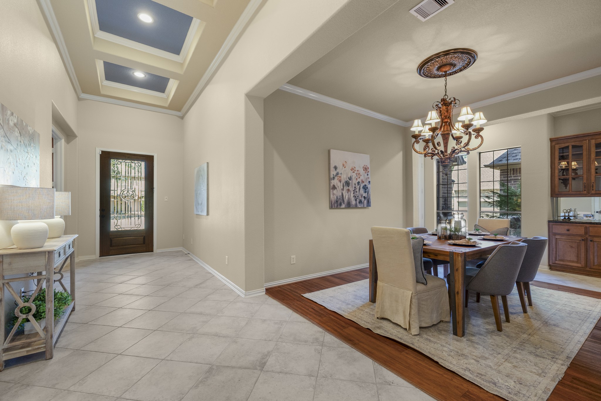 Looking back toward the front entry, the foyer highlights tray ceiling accents with crown molding, accent-color insets, and diagonal tile flooring that adds a more custom feel from the first steps inside. The study sits along the left side from this view, while the formal dining room opens to the right with warm wood flooring, creating a polished transition between the front rooms before the home continues toward the kitchen and main living spaces.