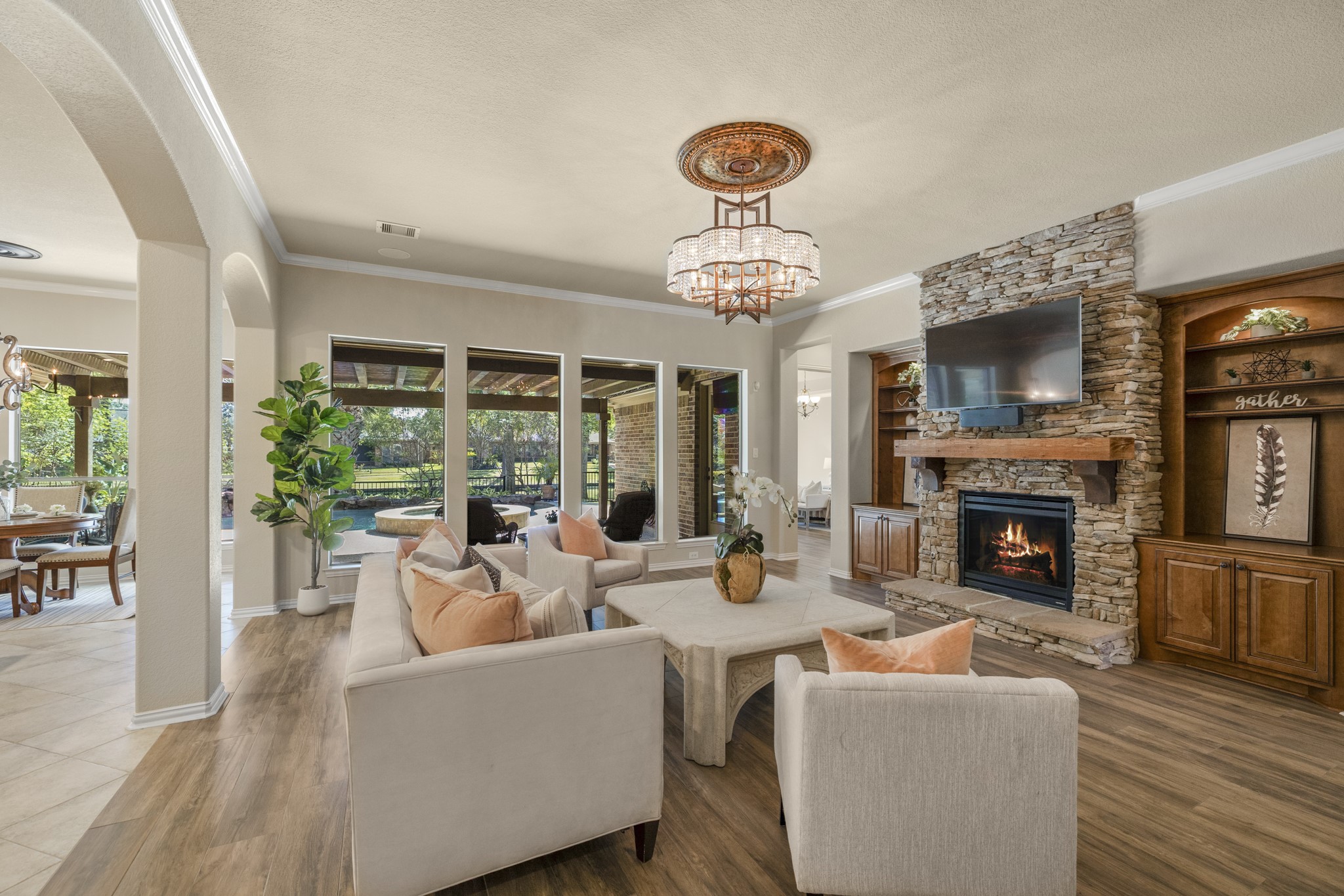From the living room, the homes indoor-outdoor lifestyle really comes through, with rear windows framing the covered pergola, pool/spa, and water-view backyard beyond. The stone fireplace and custom lighted built-ins create a warm focal point inside, while the doorway just to the right of the fireplace leads into the primary suite, guiding the walkthrough from the main gathering space into the homes private retreat.