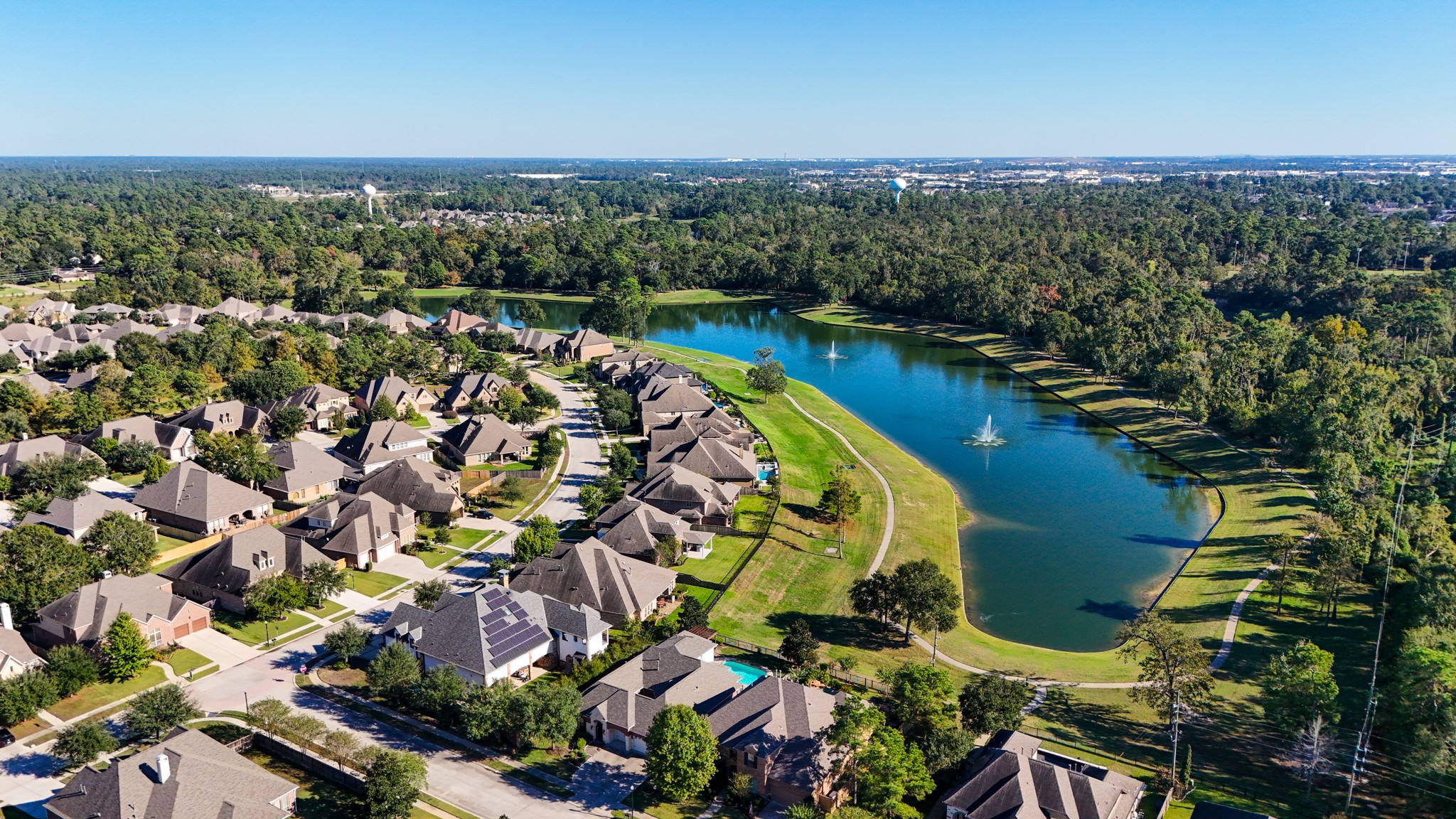 Wide aerial views show the scale of Lakes of Cypress Forest, with water, fountains, winding streets, and a wooded backdrop shaping the neighborhoods scenic feel. For buyers drawn to outdoor living, this perspective helps connect the homes poolside, water-front setting to the larger community lifestyle of lakes, paths, and green space.