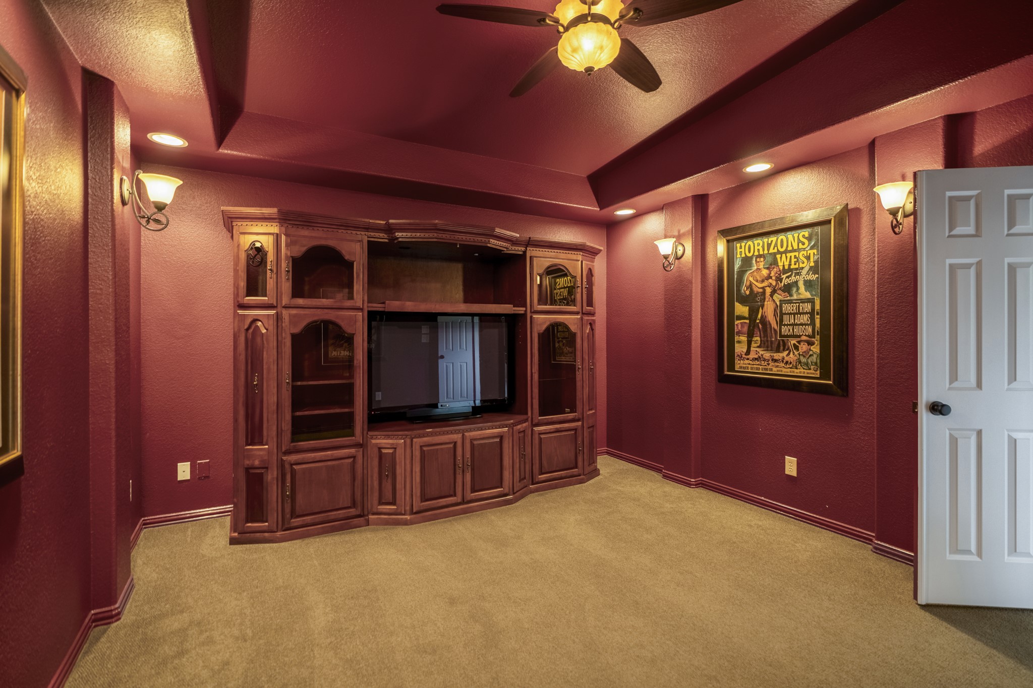 Inside the media room, the upstairs retreat shifts into a true movie-night setting with deeper wall color, a ceiling fan, and built-in glass-front cabinetry that gives the room a finished, lounge-like feel. Positioned just off the game room, this space keeps entertainment upstairs with the nearby half bath close by, creating a separate level for watching, playing, and unwinding.