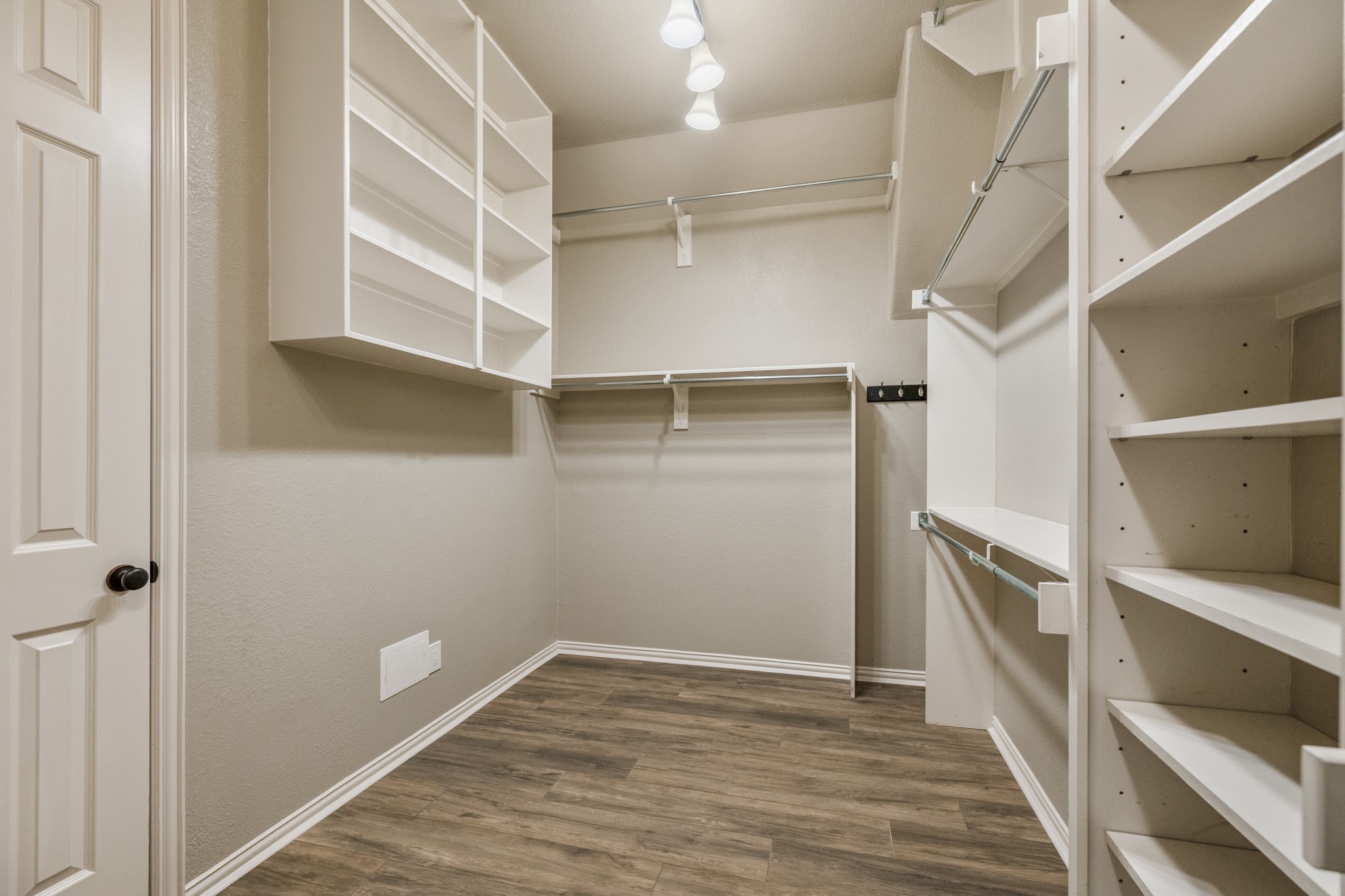 Another view of the primary walk-in closet shows the storage continuing with built-in shelving, hanging space, and wide-plank wood-look tile carried through from the suite. The doorway on the left leads back toward the remodeled primary bath, keeping the closet connected to the bath and bedroom for a smooth, private flow within the primary retreat.