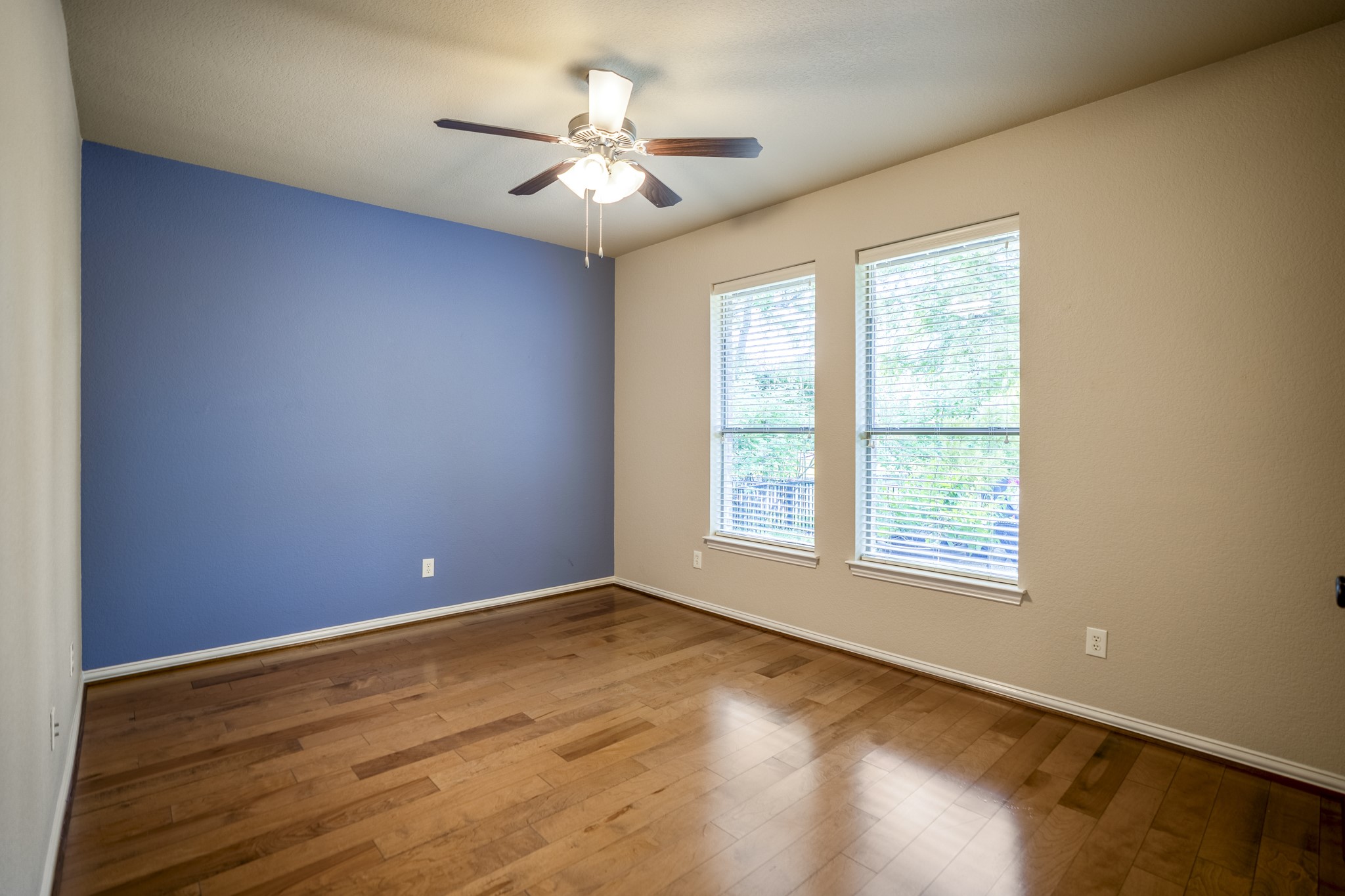 Moving toward the back of the home near the breakfast nook, this third bedroom brings in natural light through two windows and continues the homes more custom feel with warm wood flooring and a blue accent wall. Its location near the rear bedroom hall keeps these additional bedrooms close to the kitchen and breakfast area while still set apart from the main living room flow.