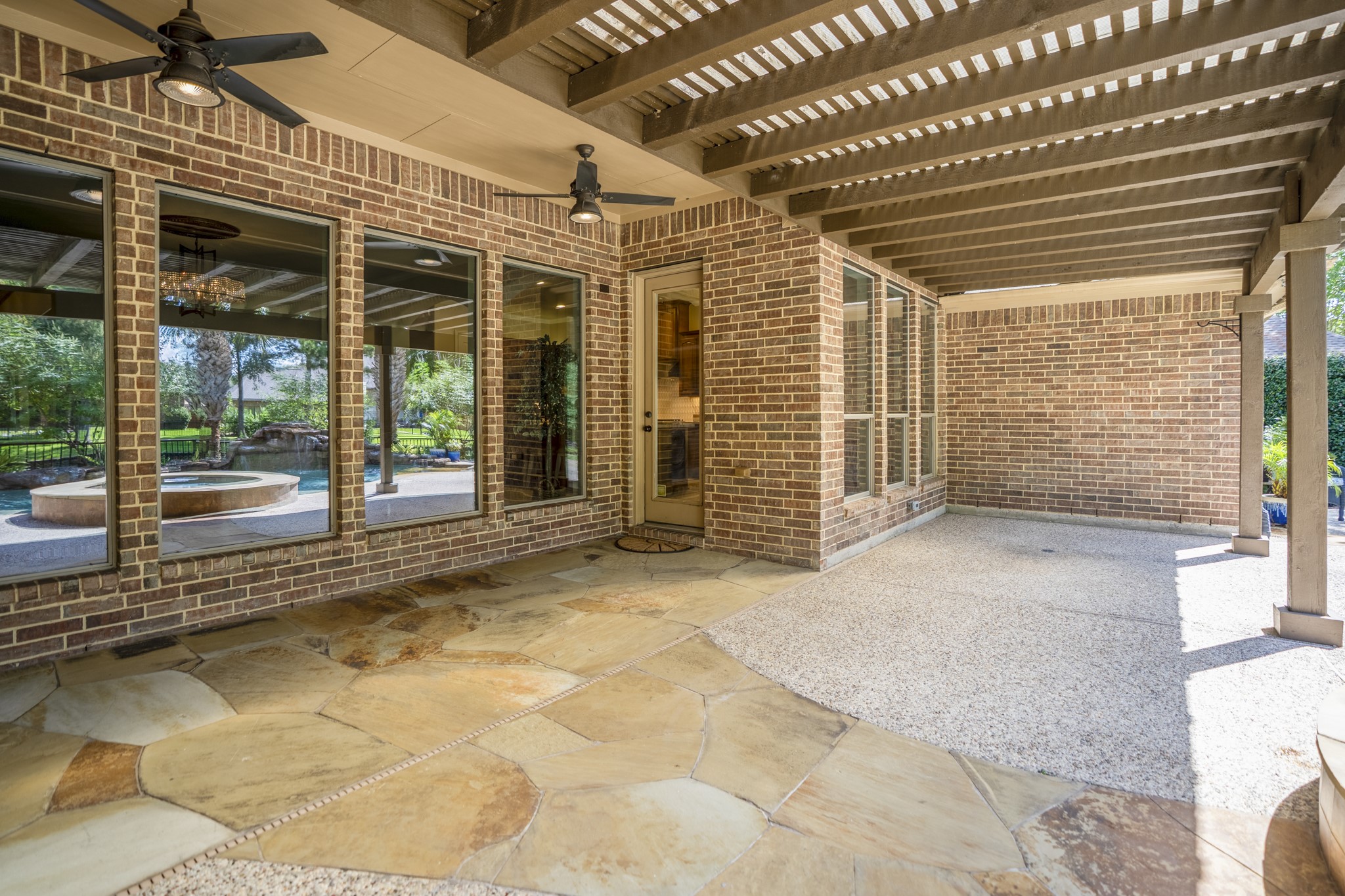 Beneath the 30 covered pergola, the back patio feels like an outdoor living space made for shaded afternoons, rainy-day coverage, and slower evenings by the water. Stone flooring, substantial support posts, and the covered structure extend the homes living space outside, while the windows and doors keep the patio connected to the living room and breakfast nook just inside.